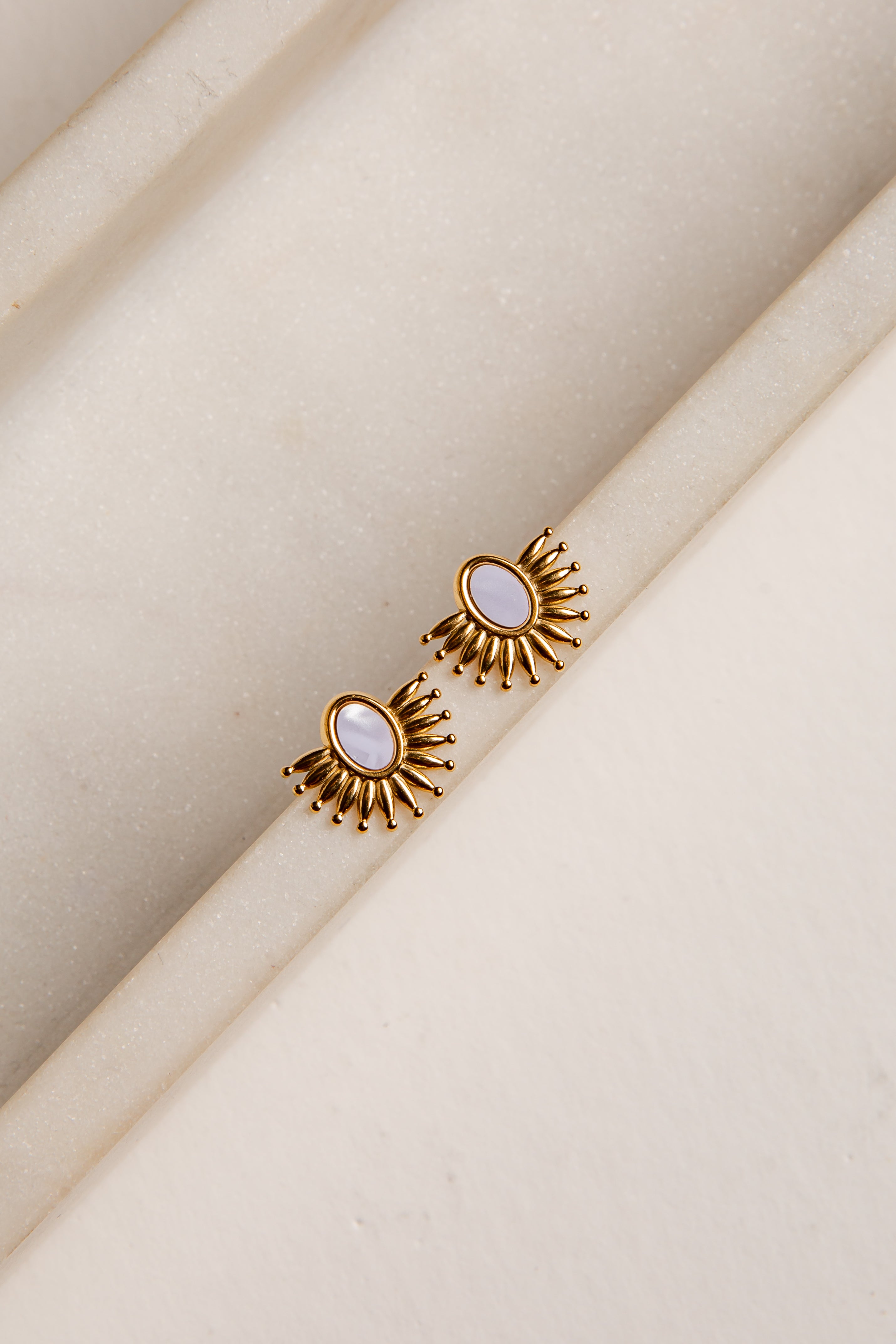 Gold earrings with a central gemstone on a beige fabric background