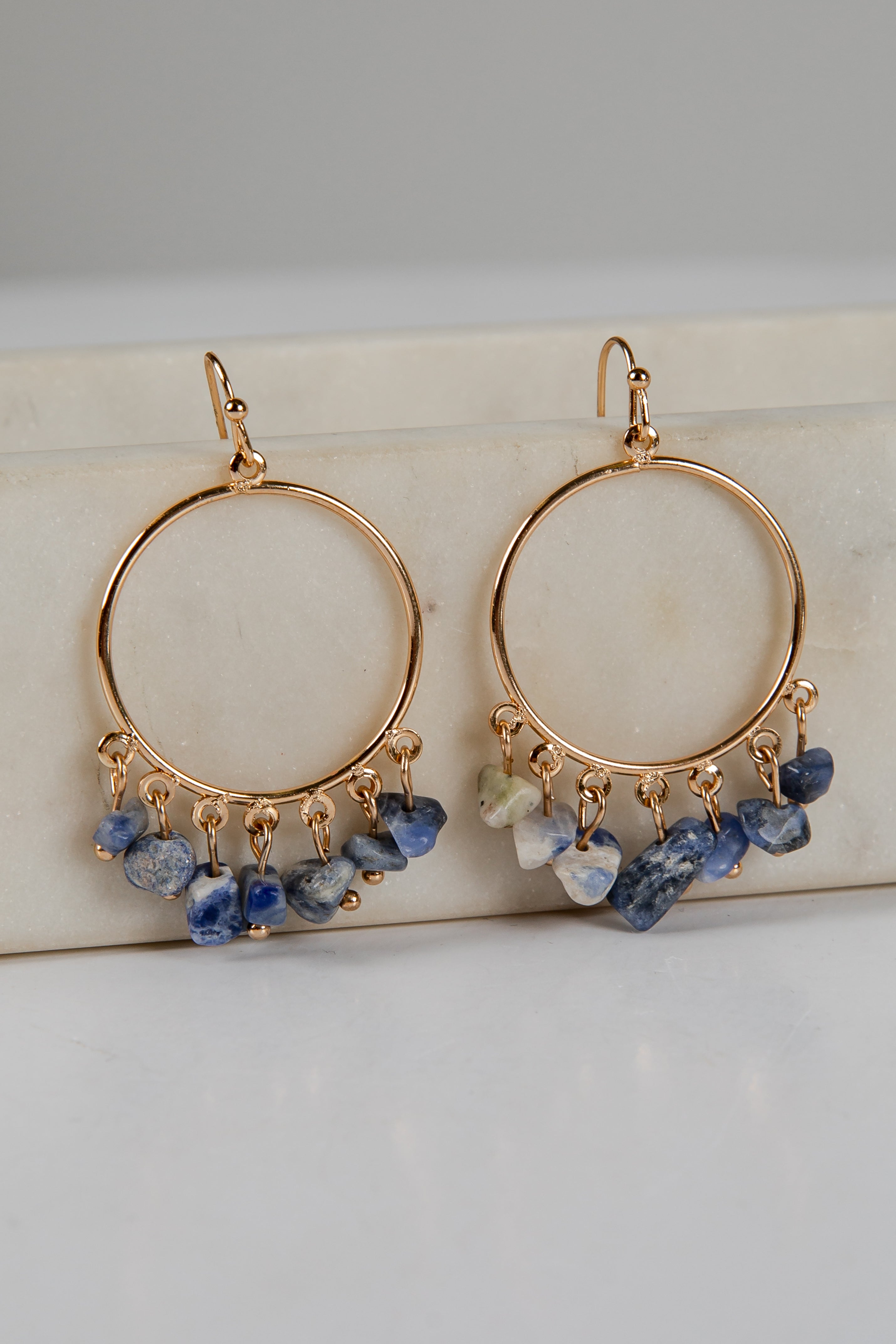 Gold hoop earrings with blue and green gemstone drops on a light background