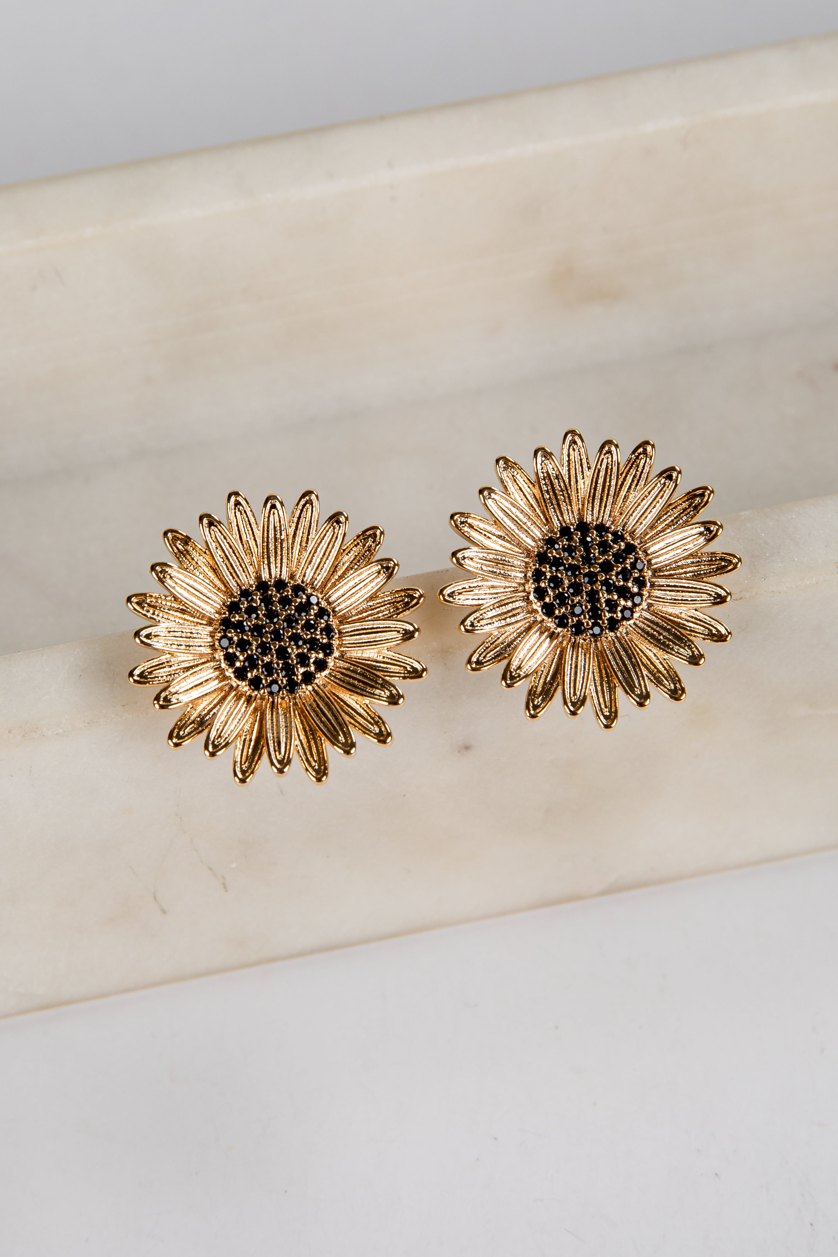 Gold sunflower-shaped earrings on a light beige surface