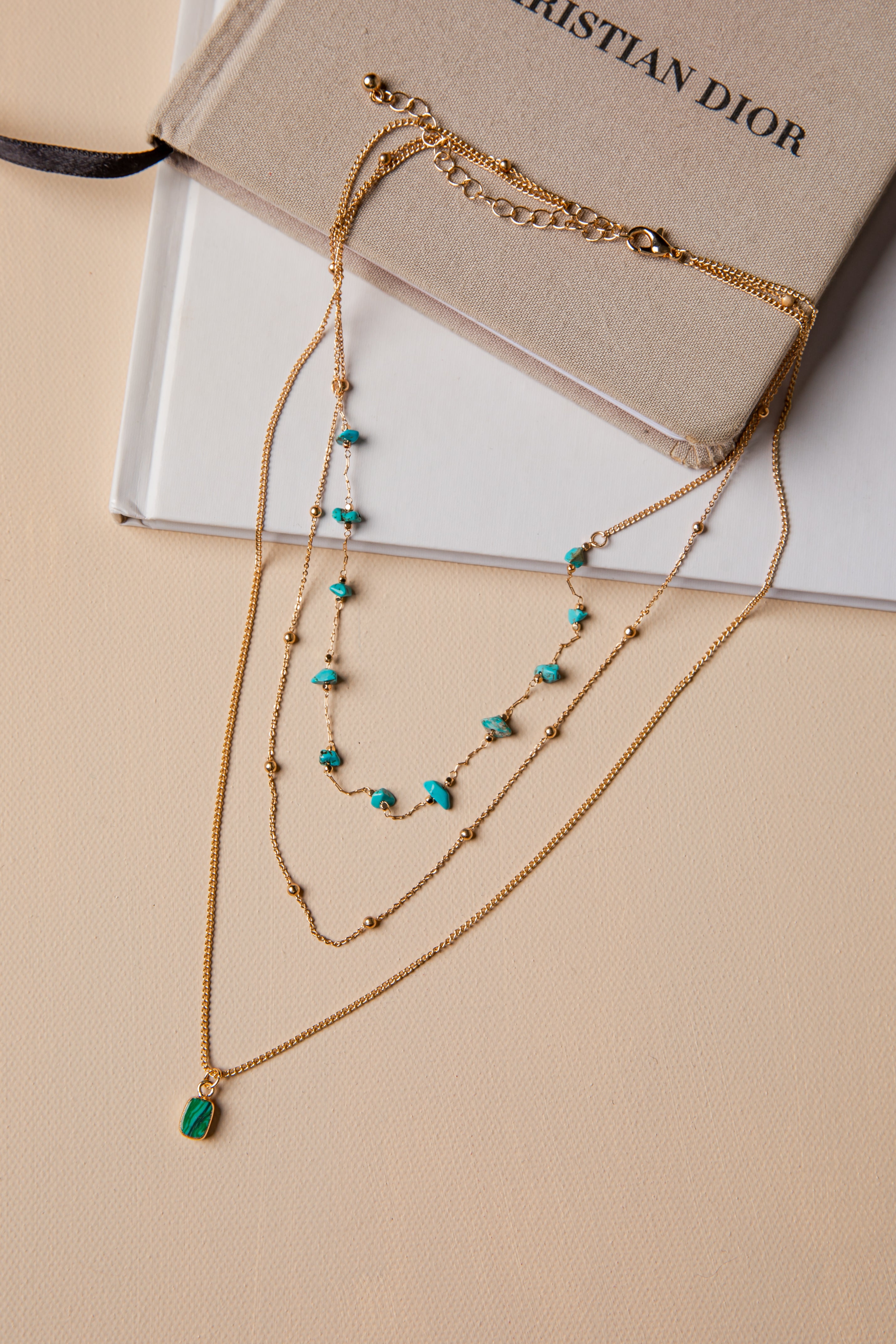 Gold necklace with green stones on a beige surface with a Christian Dior book in the background