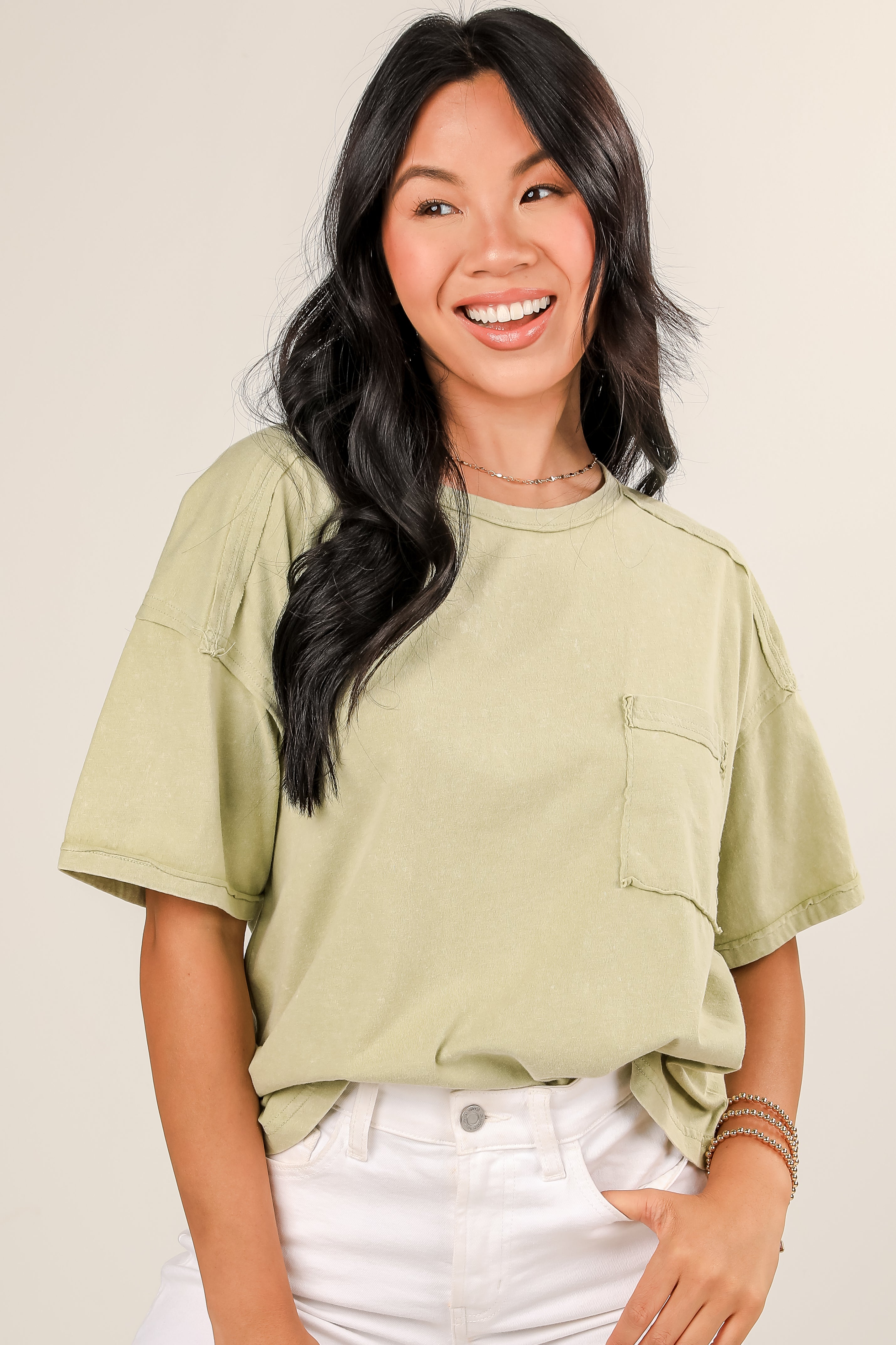 Woman wearing a light green t-shirt and white pants against a beige background