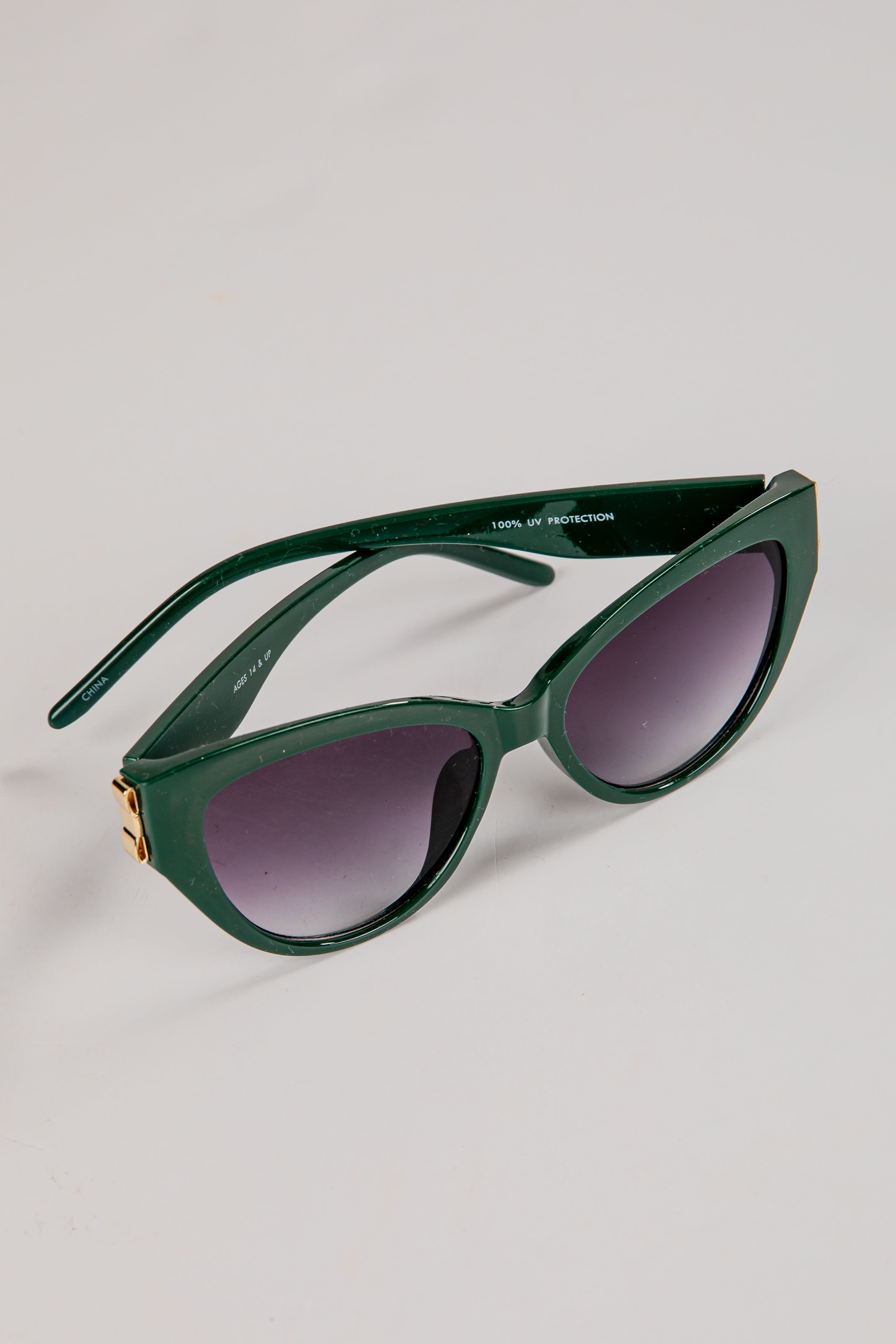 Green sunglasses with dark lenses on a light gray background