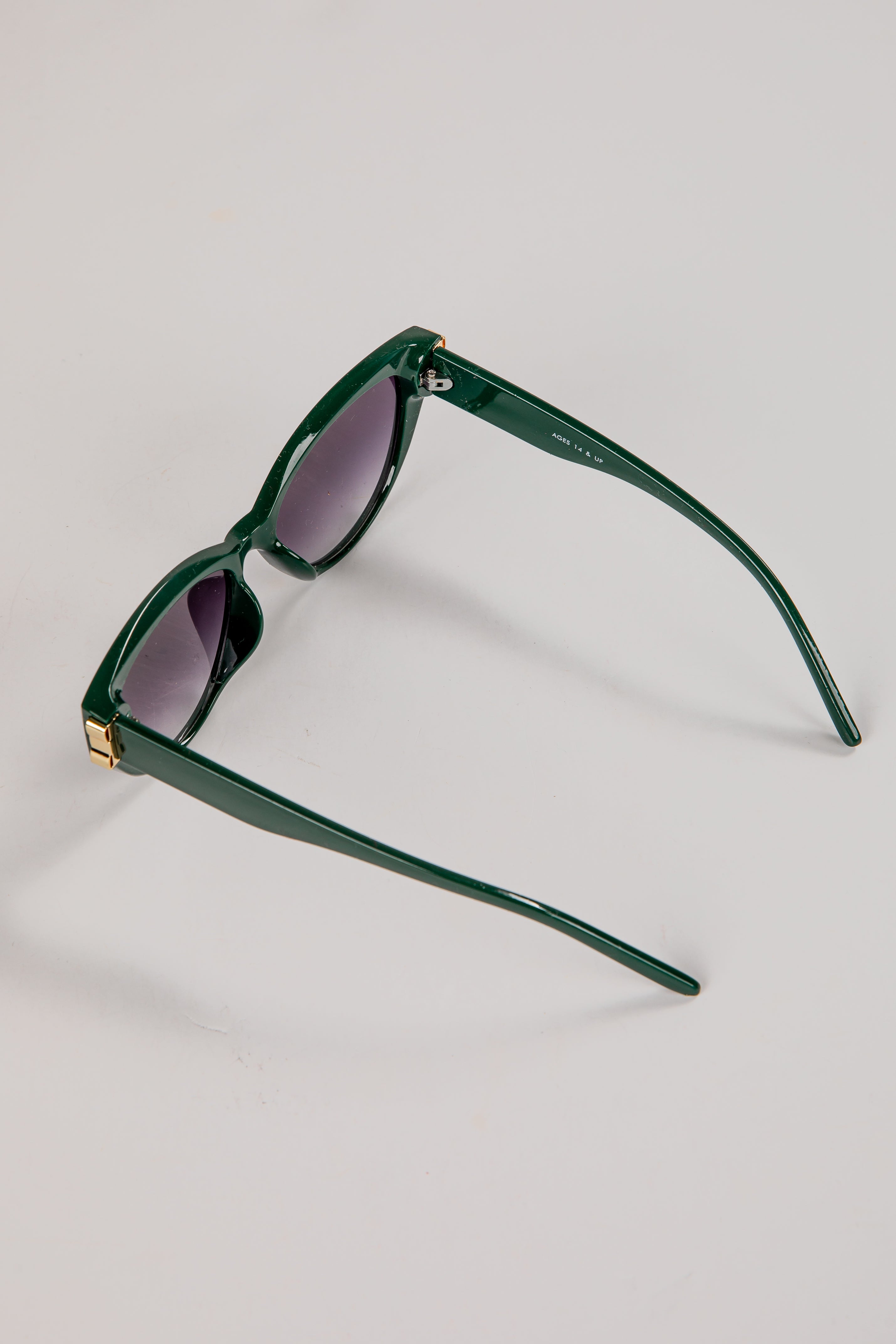 Green sunglasses with a gold accent on a light gray background