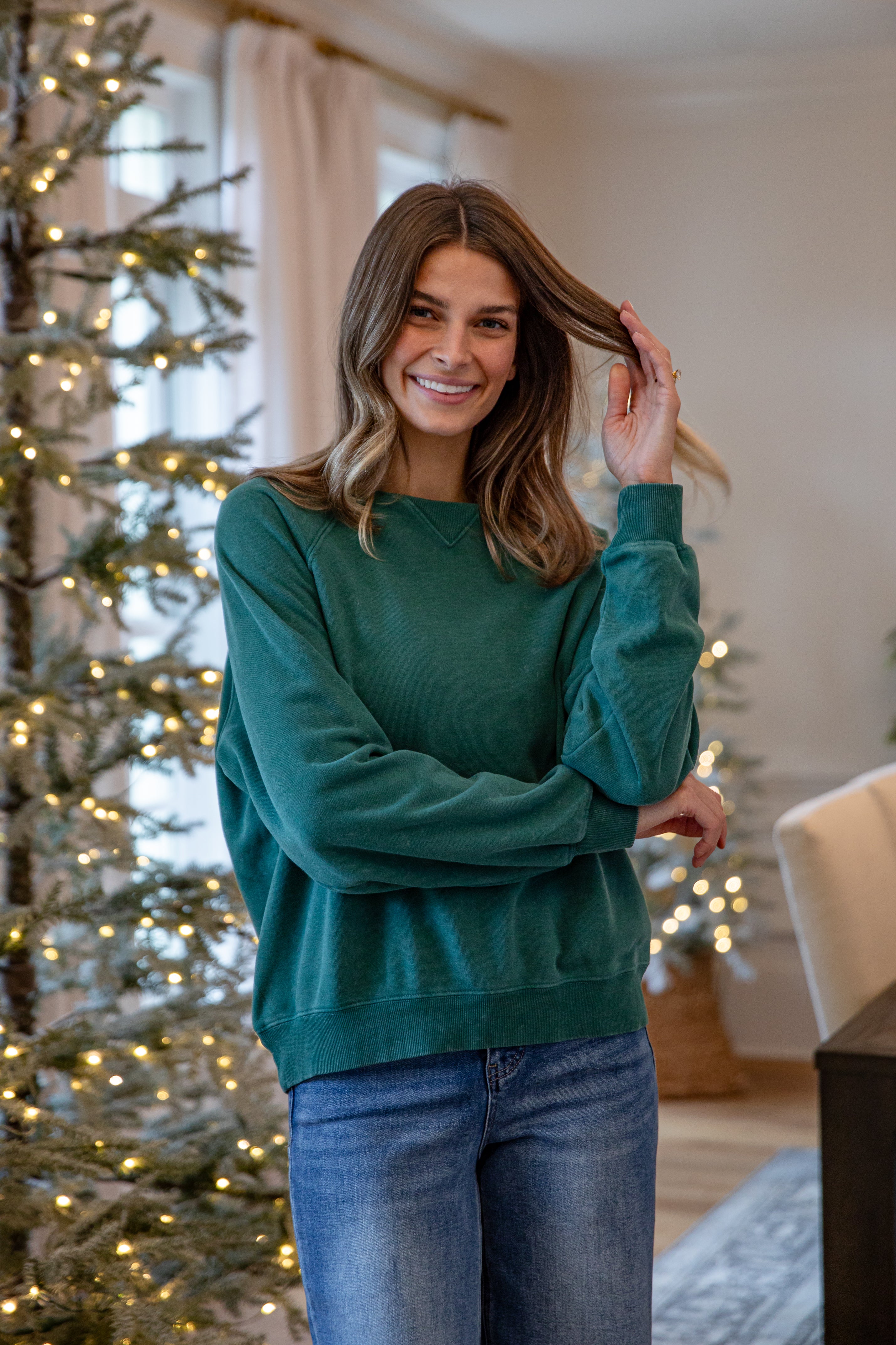 Woman in a green sweater standing in a room with Christmas trees.