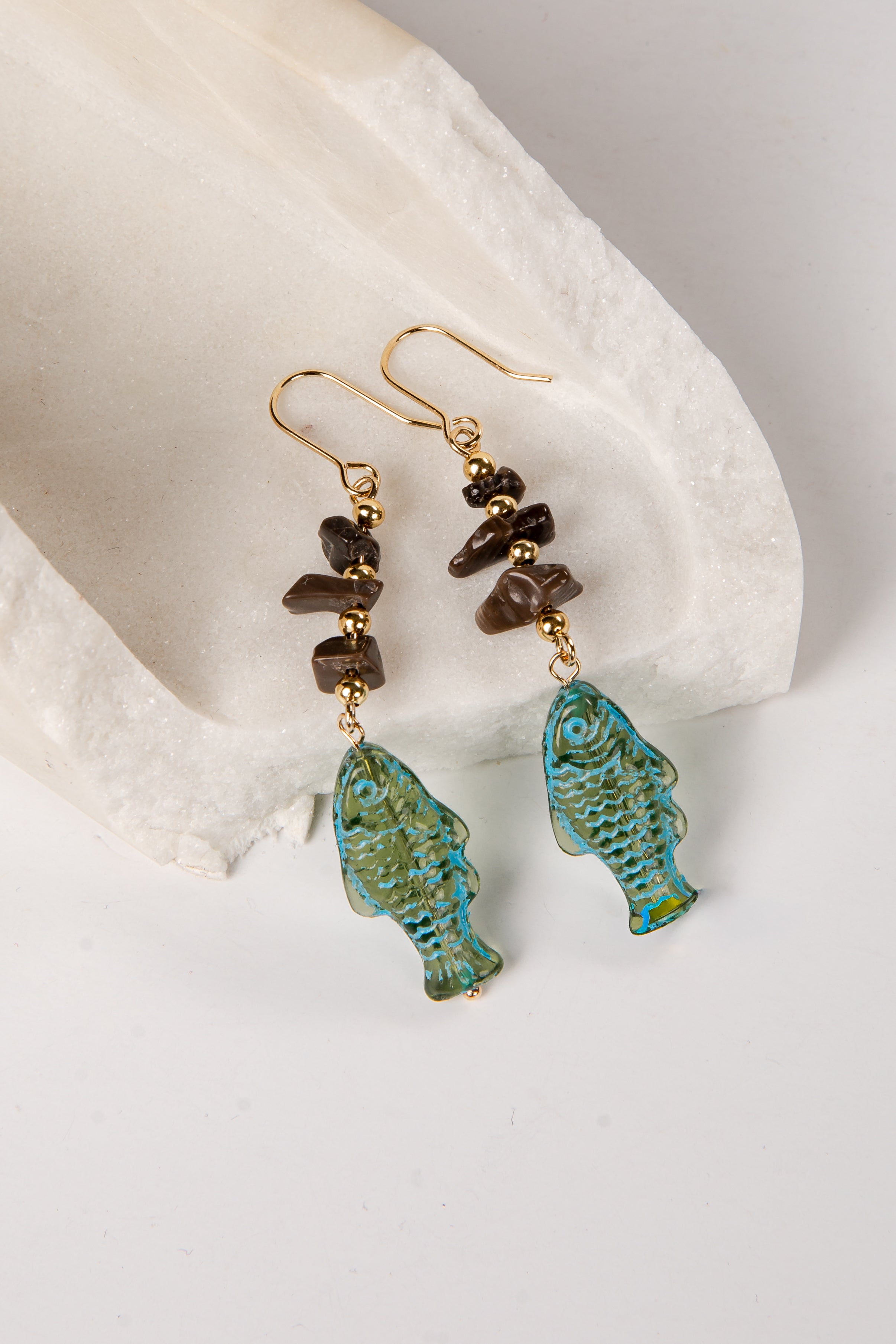 Pair of earrings with turquoise fish-shaped drops and brown beads on a white stone background