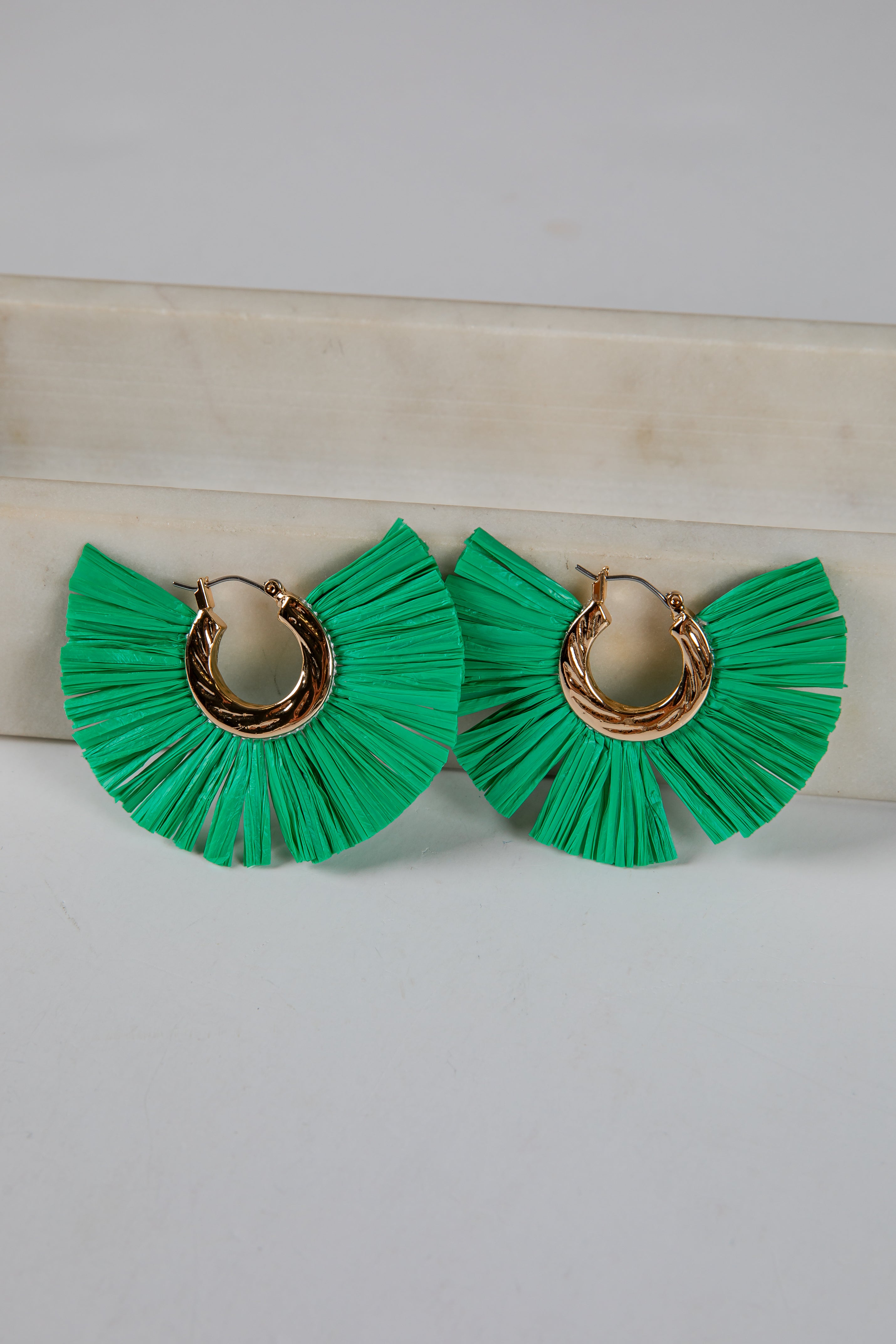 Green ruffled earrings with gold hoops on a light background