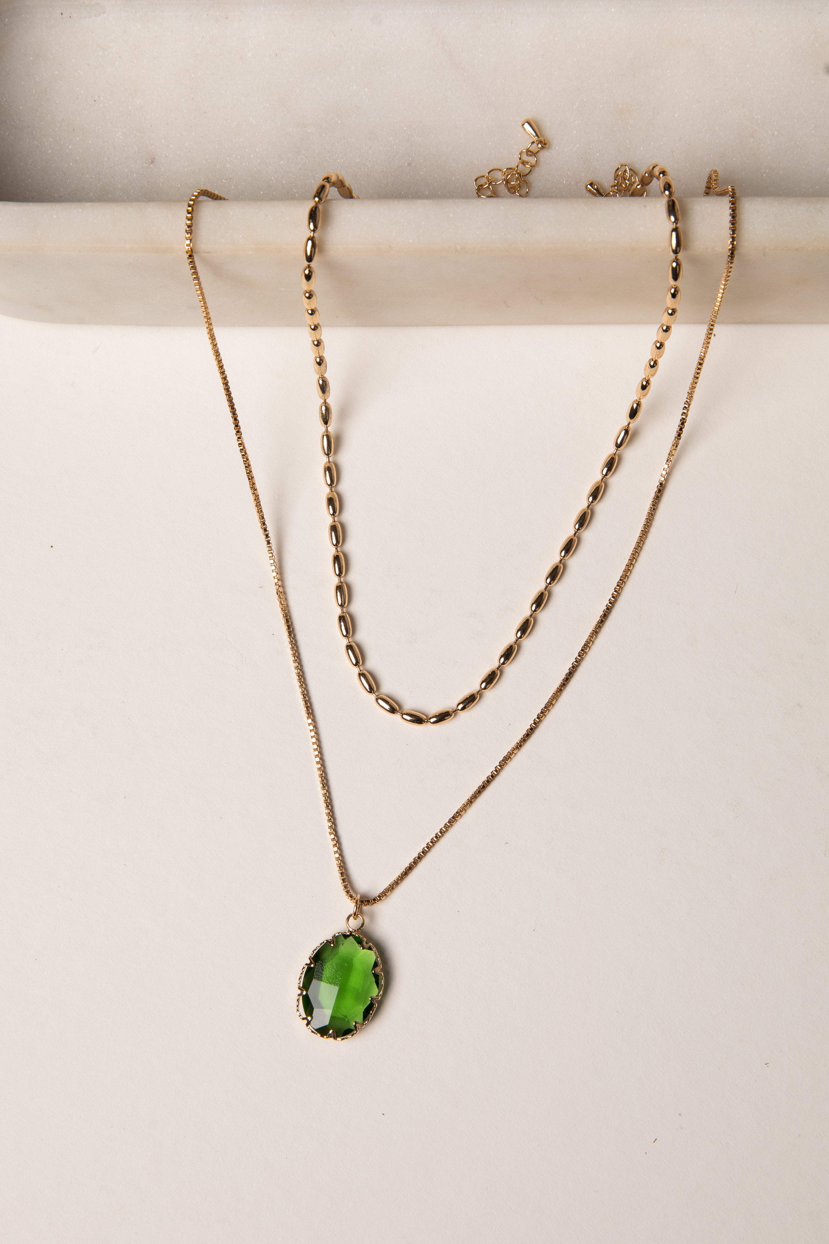 Two gold necklaces with green pendants on a white background