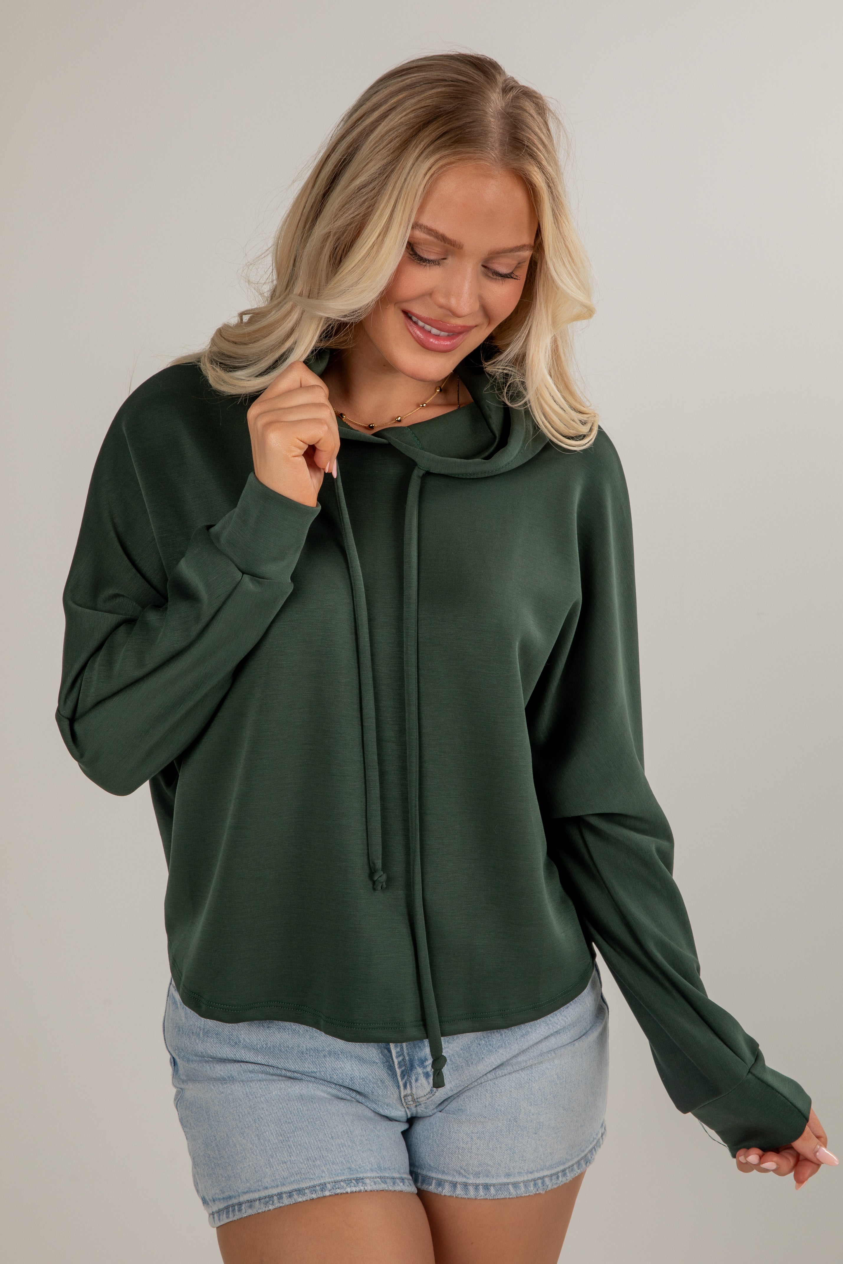 Woman wearing a green hoodie and denim shorts on a plain background