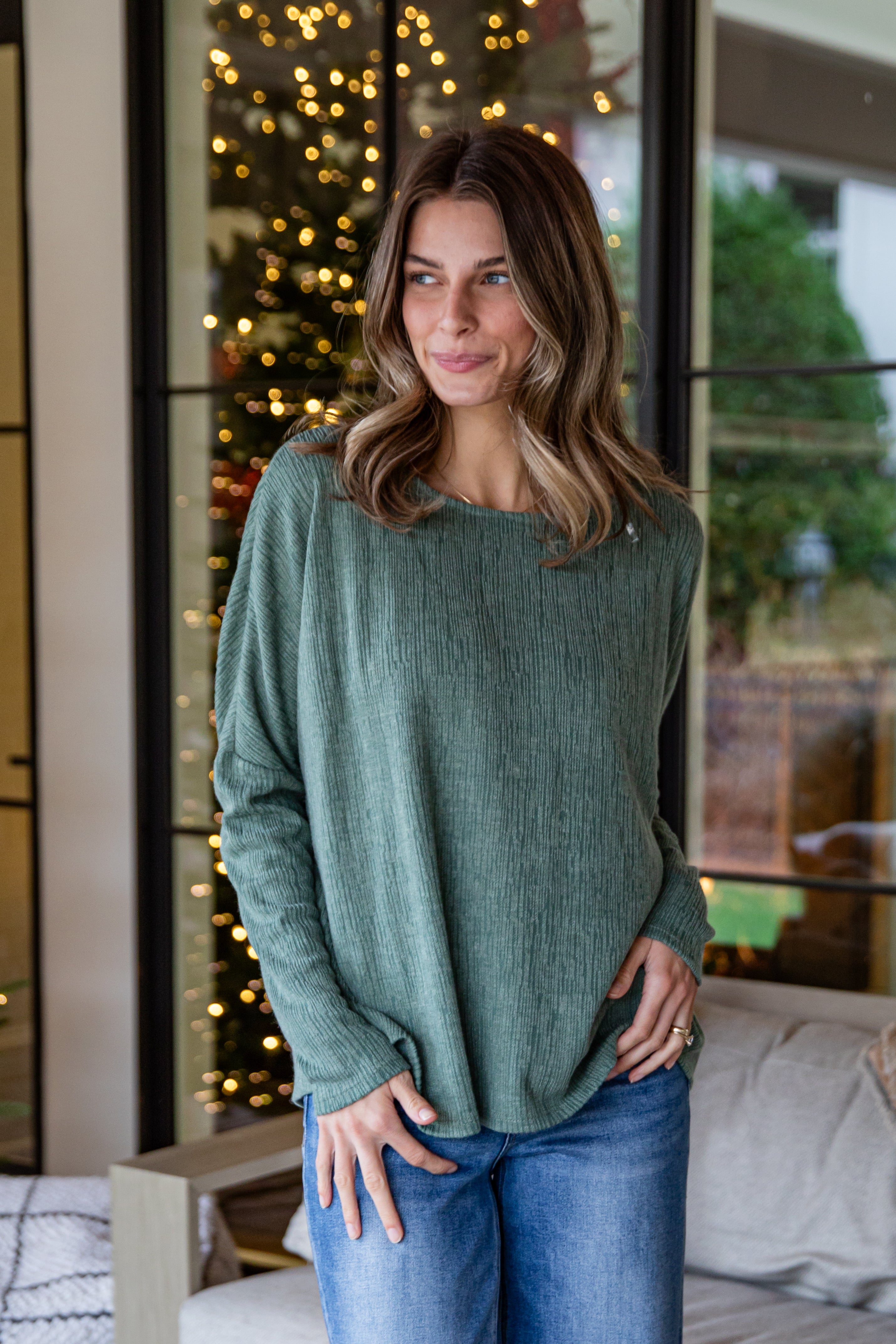 Woman wearing a green sweater and blue jeans standing in a room with decorative lights.
