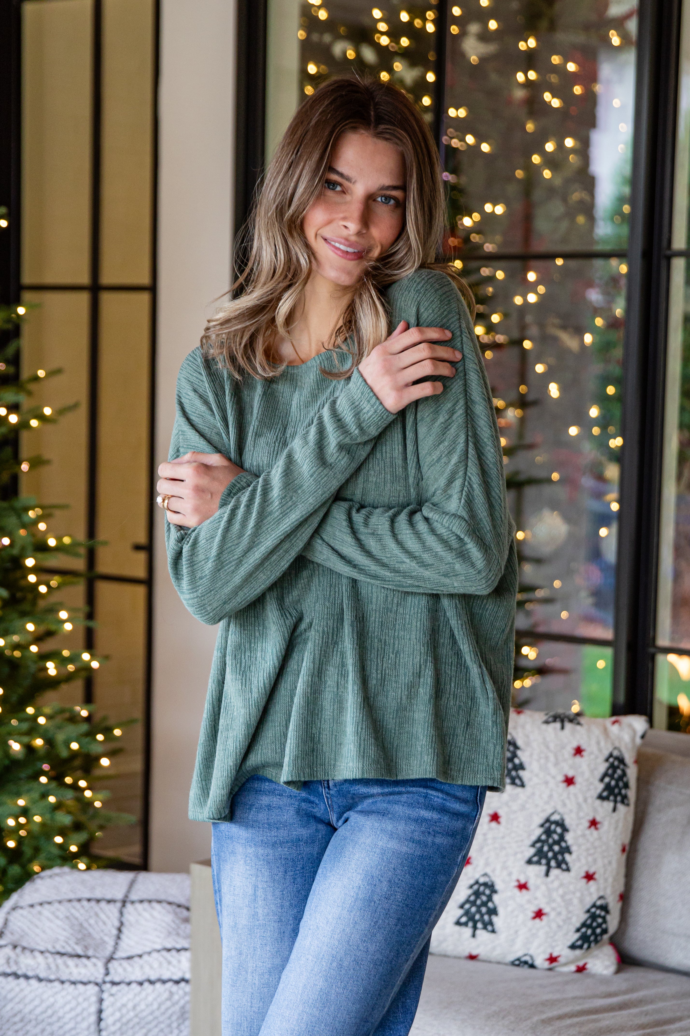 Woman wearing a green sweater and blue jeans standing in a room with Christmas decorations.