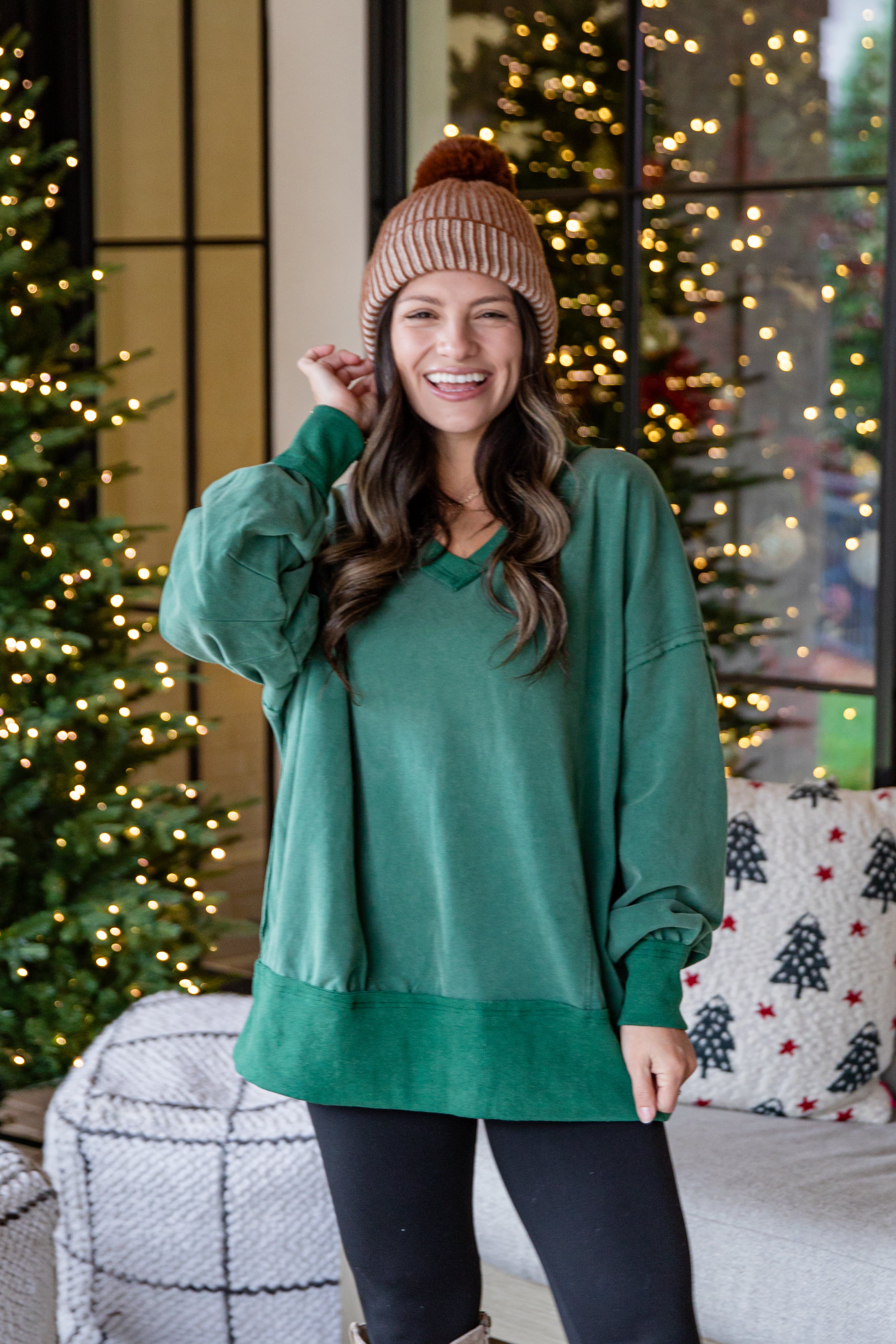 Woman wearing a green sweater and brown beanie in front of Christmas trees.