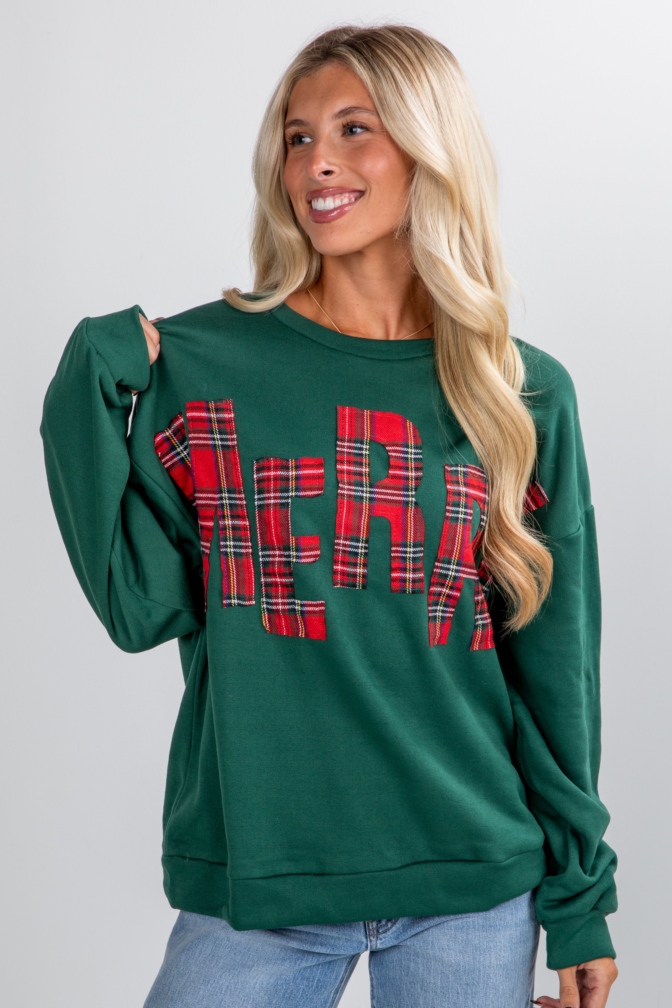 Woman wearing a green sweatshirt with plaid lettering on a plain background