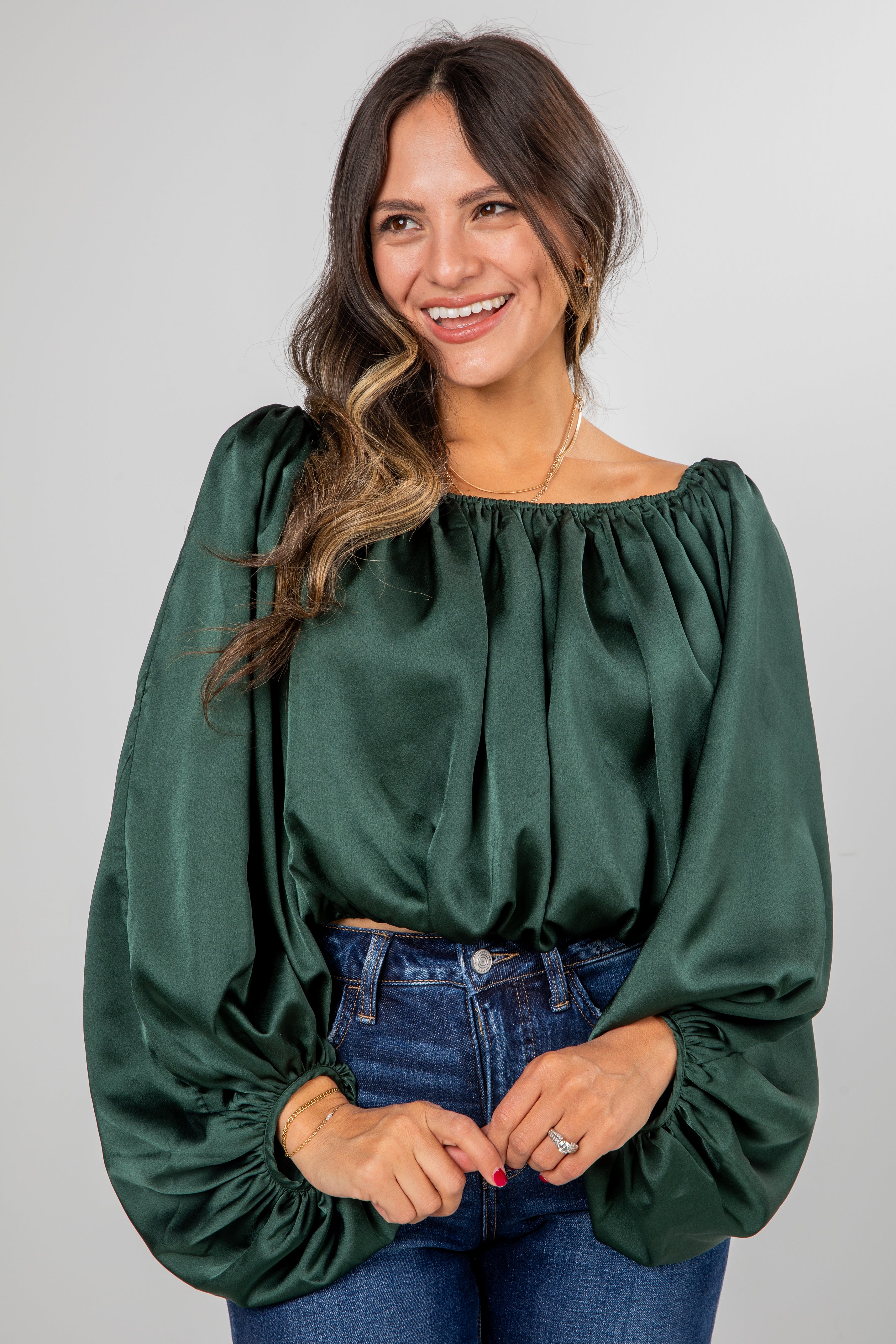Woman wearing a green blouse with long sleeves against a gray background