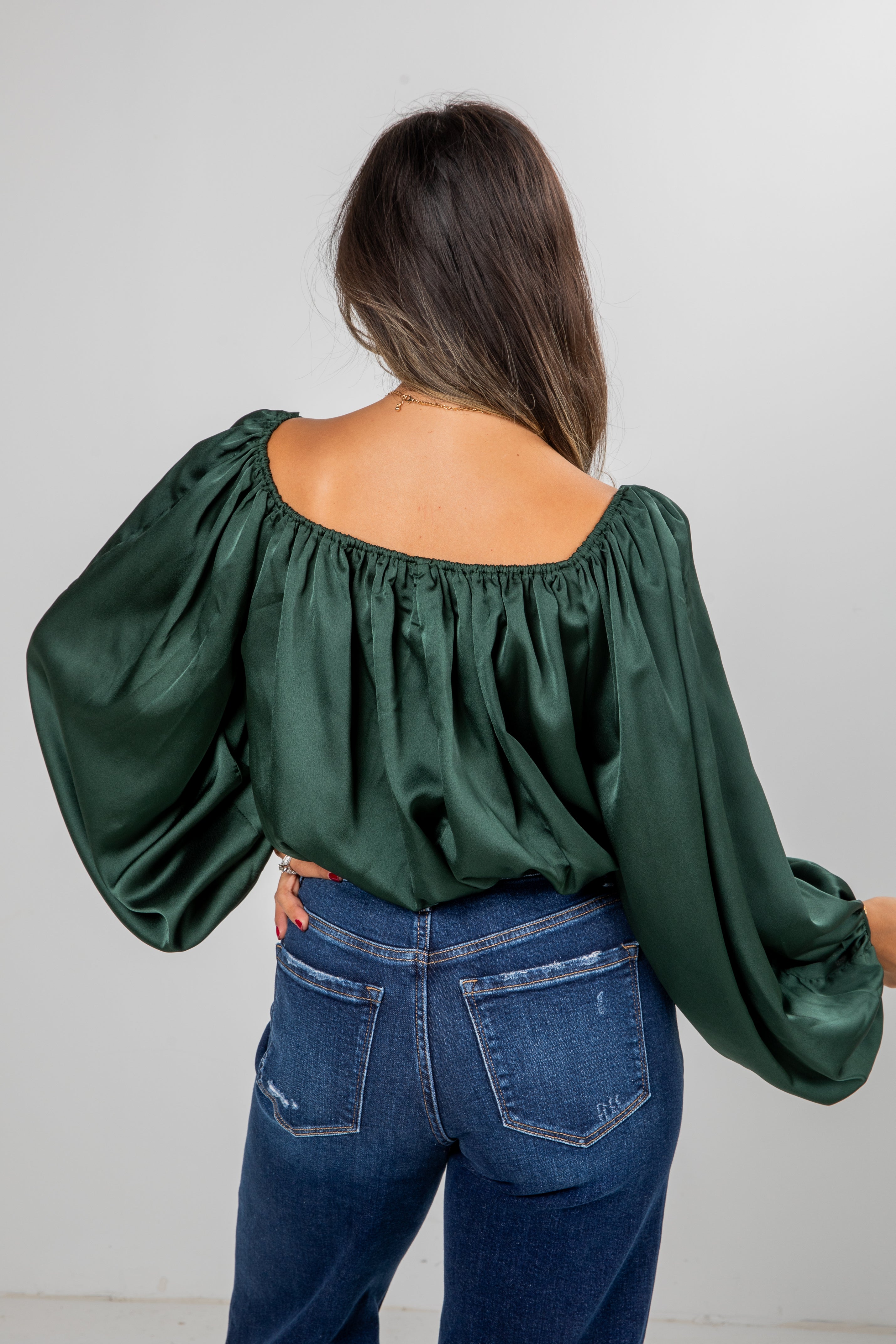 Person wearing a green blouse with puffed sleeves and blue jeans against a plain background
