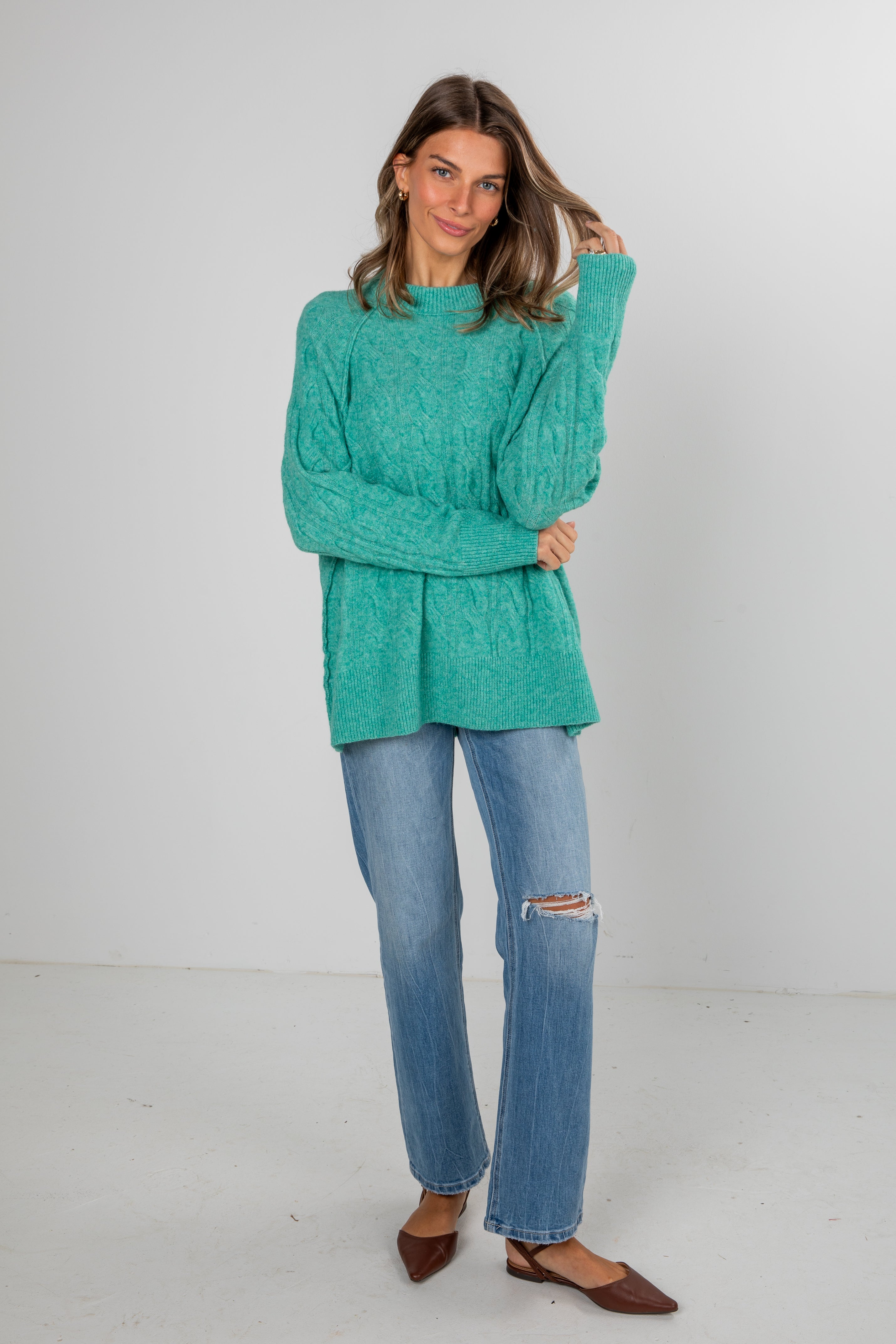 Woman wearing a teal sweater and blue jeans on a white background