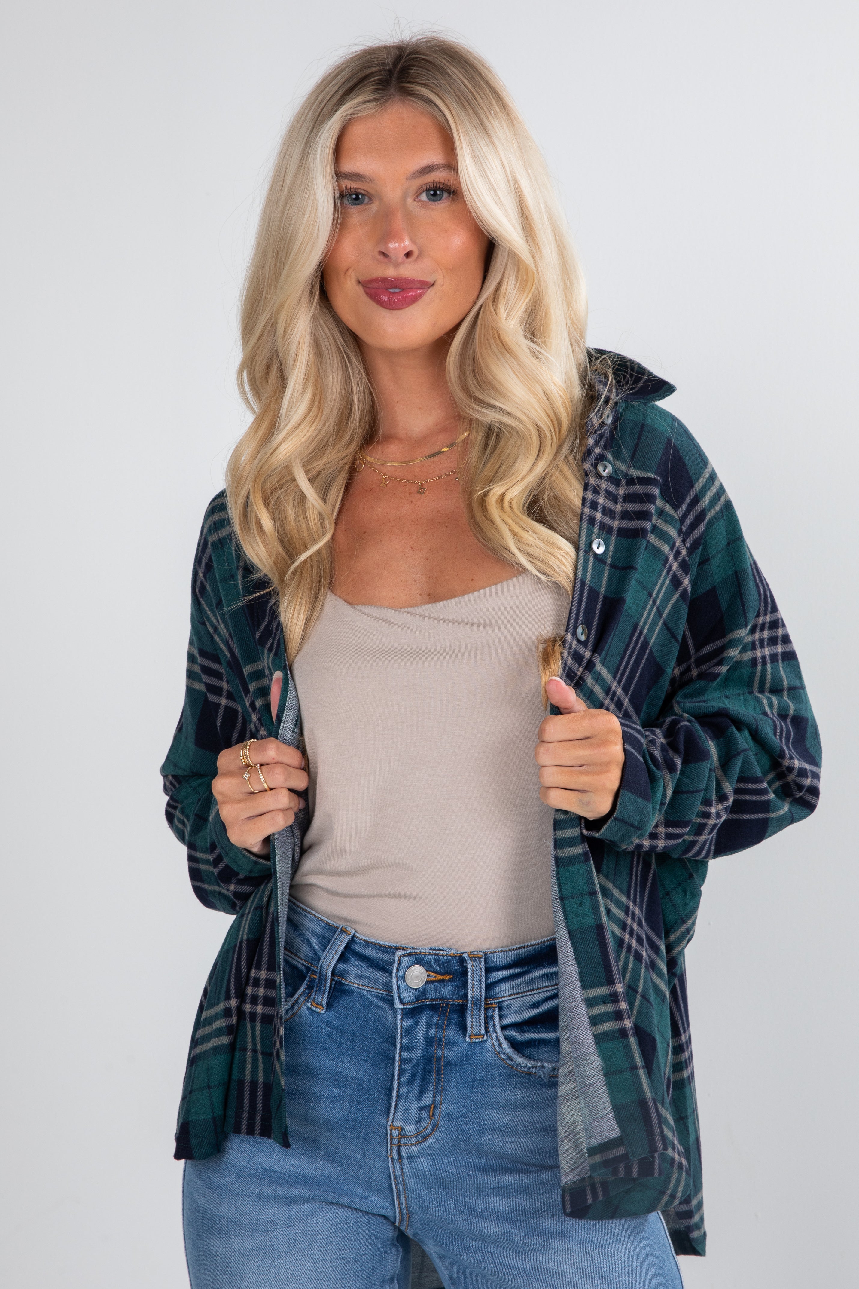 Woman wearing a plaid shirt over a beige top and jeans on a white background