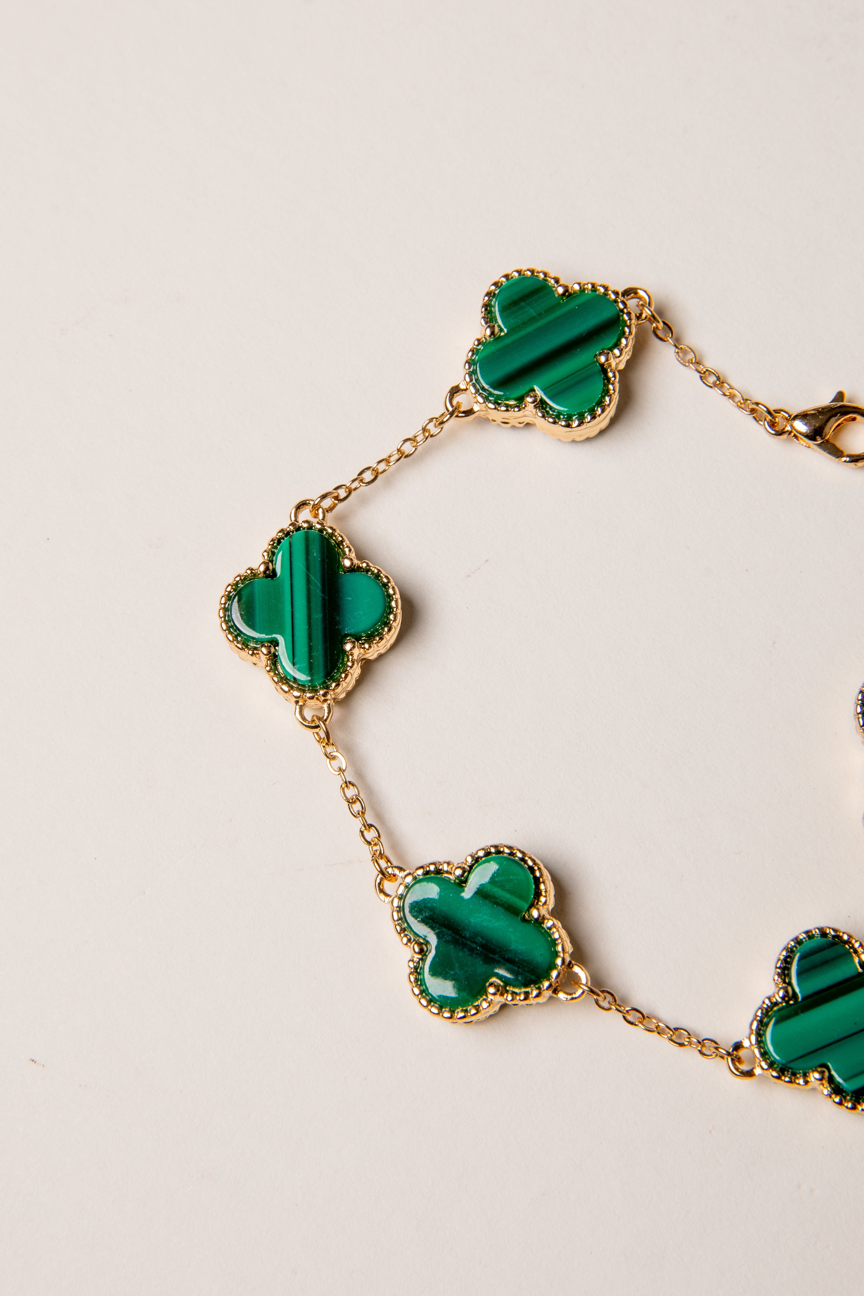 Gold bracelet with green clover-shaped charms on a light background