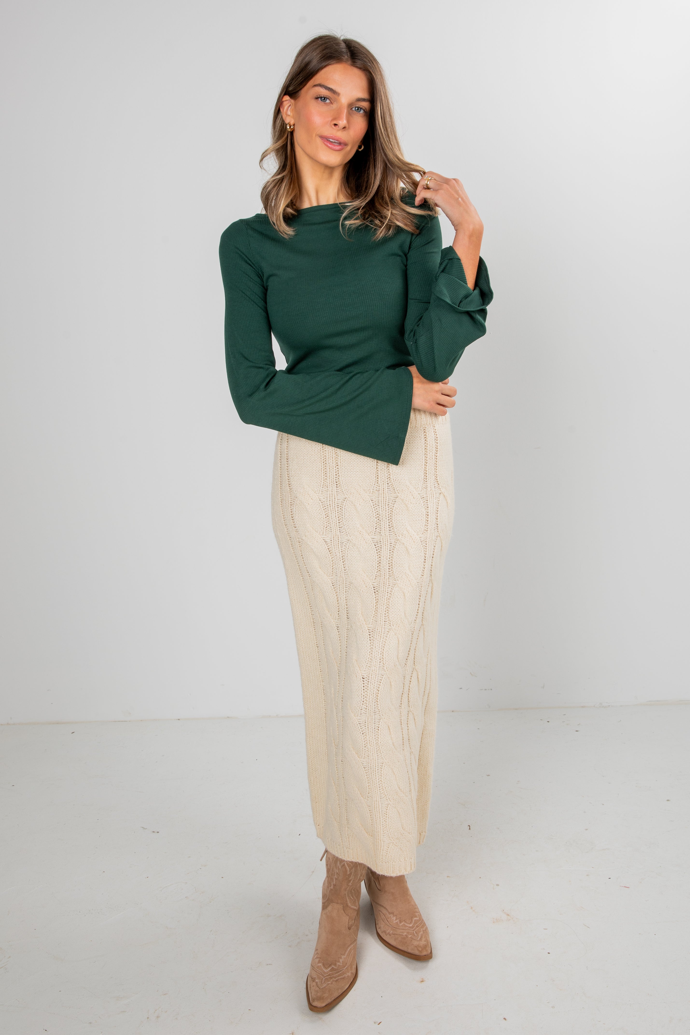 Woman wearing a green top and beige pants on a white background