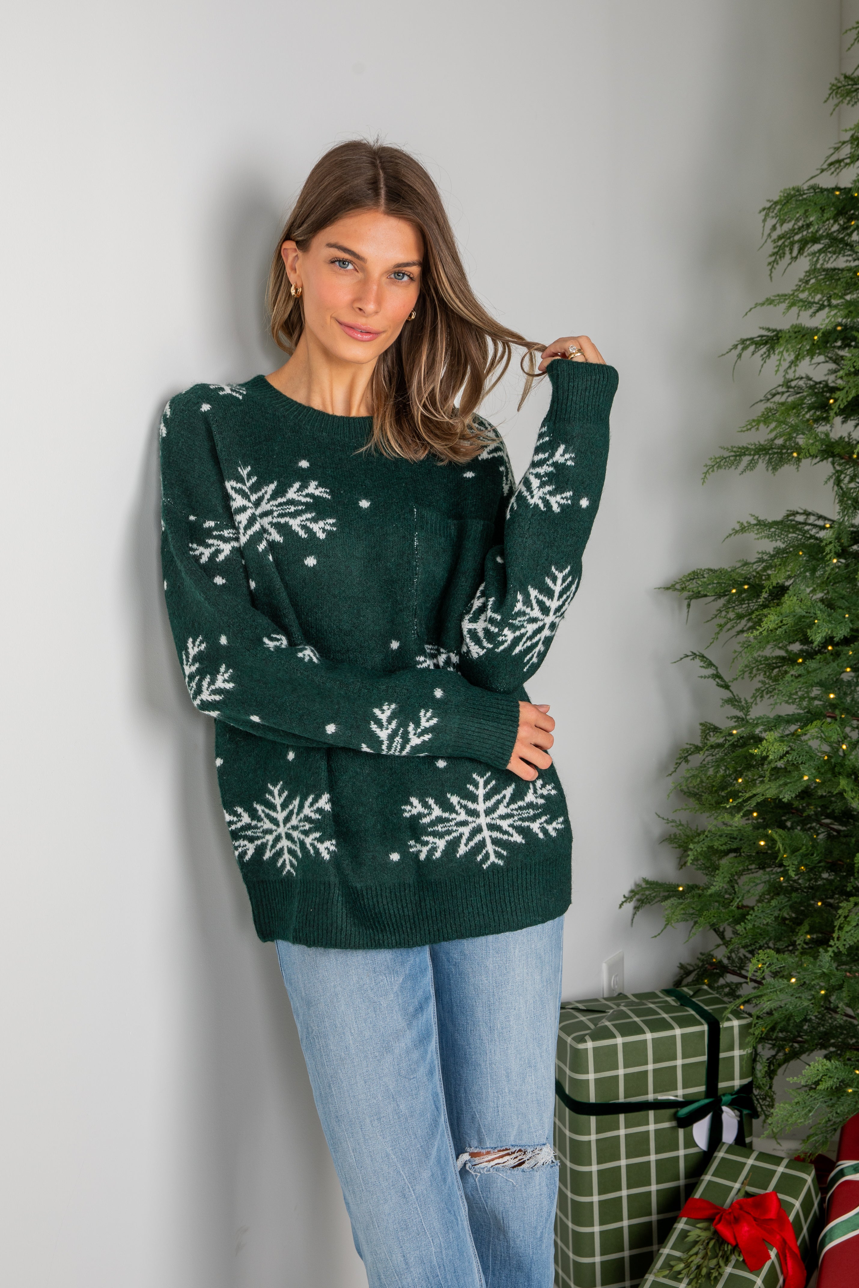 Woman wearing a green sweater with snowflake patterns in front of a Christmas tree and presents.