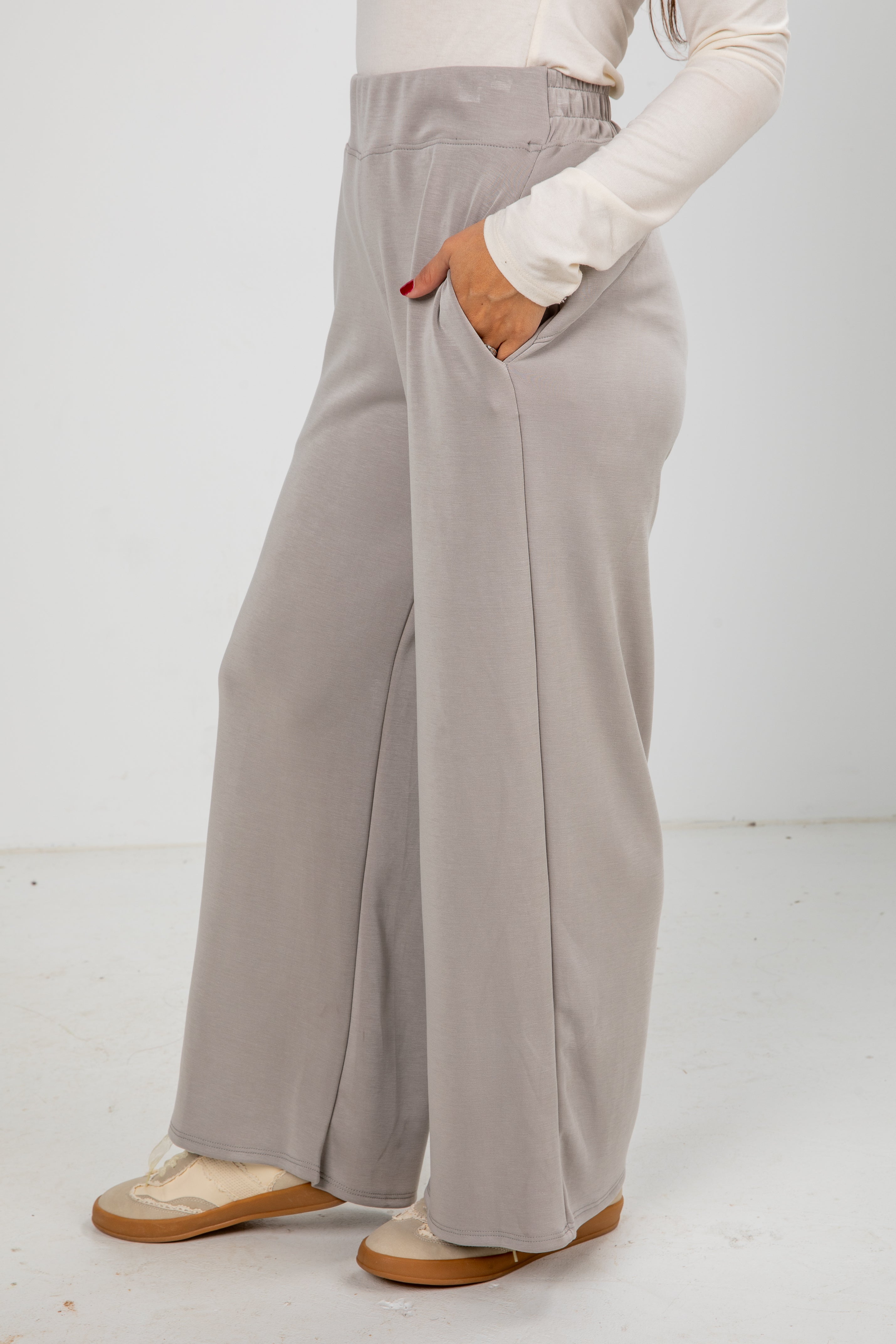 Person wearing light gray wide-leg pants with a white top on a white background