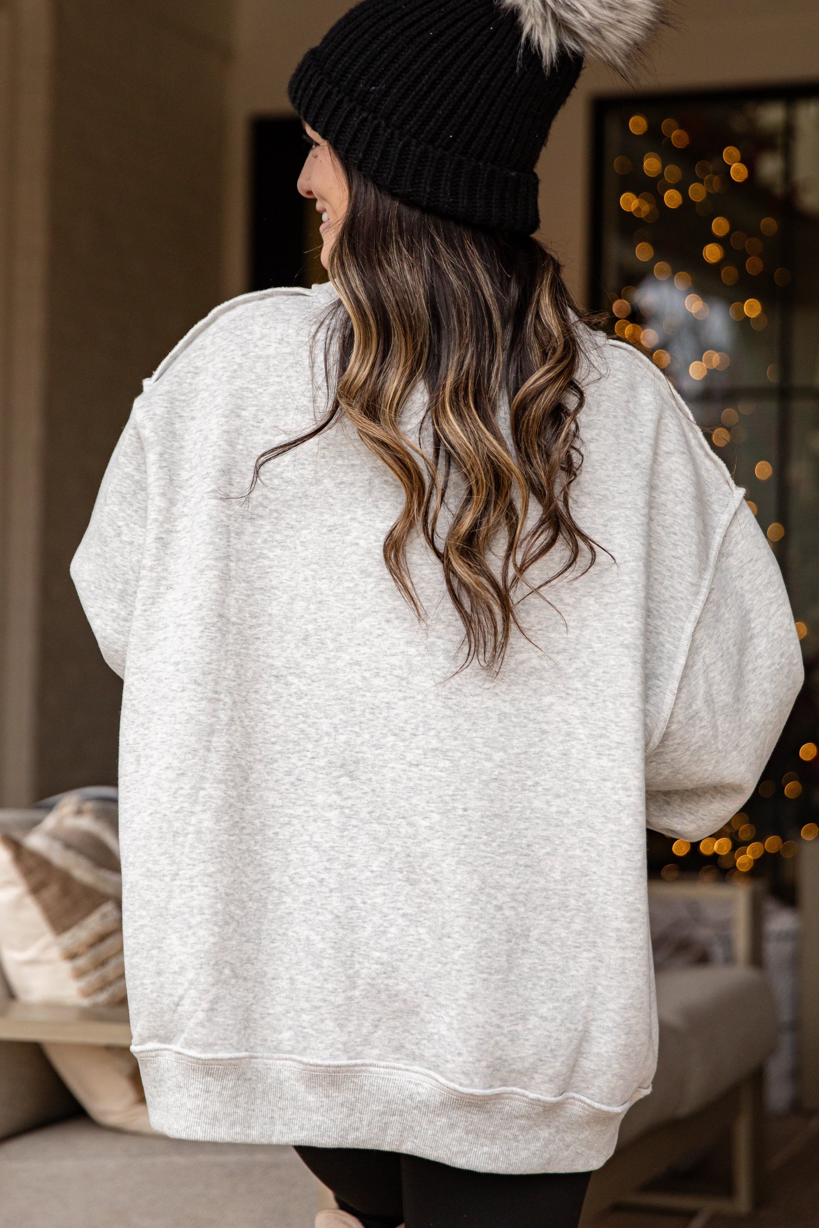 Person wearing a white oversized sweater and black beanie in a cozy indoor setting with blurred lights.