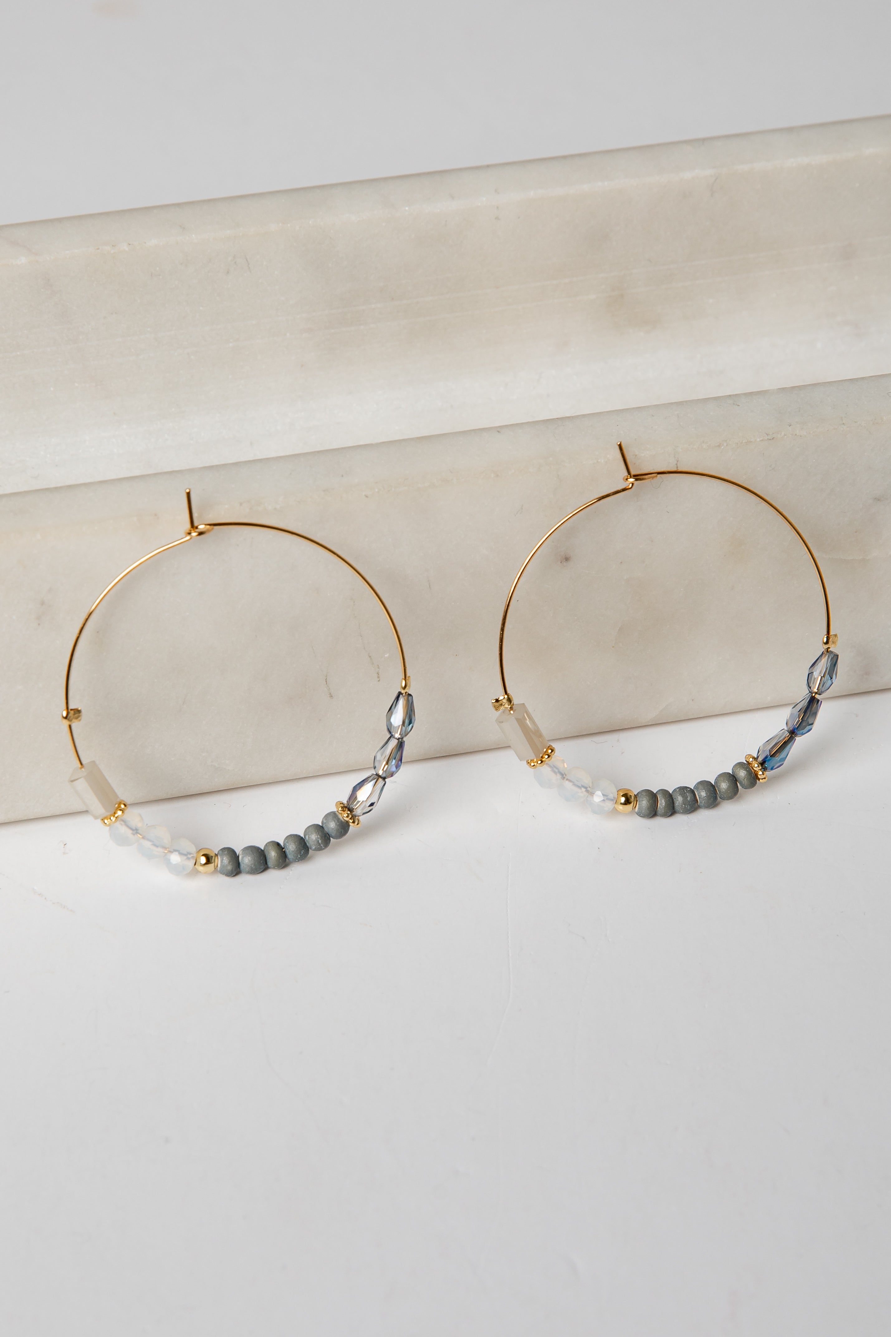 Gold hoop earrings with gray beads on a marble surface