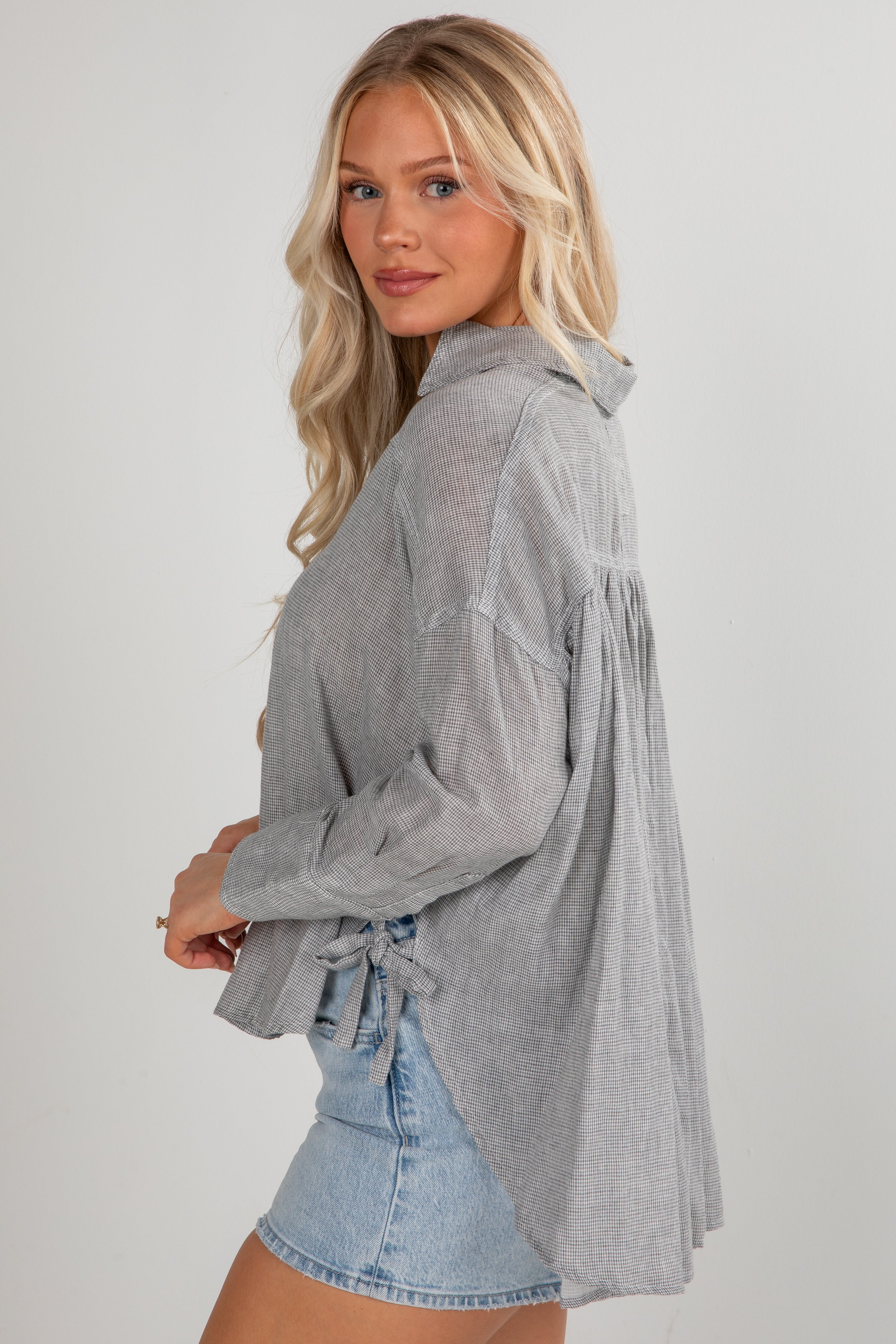 Woman wearing a gray long-sleeve shirt with a denim skirt on a plain background