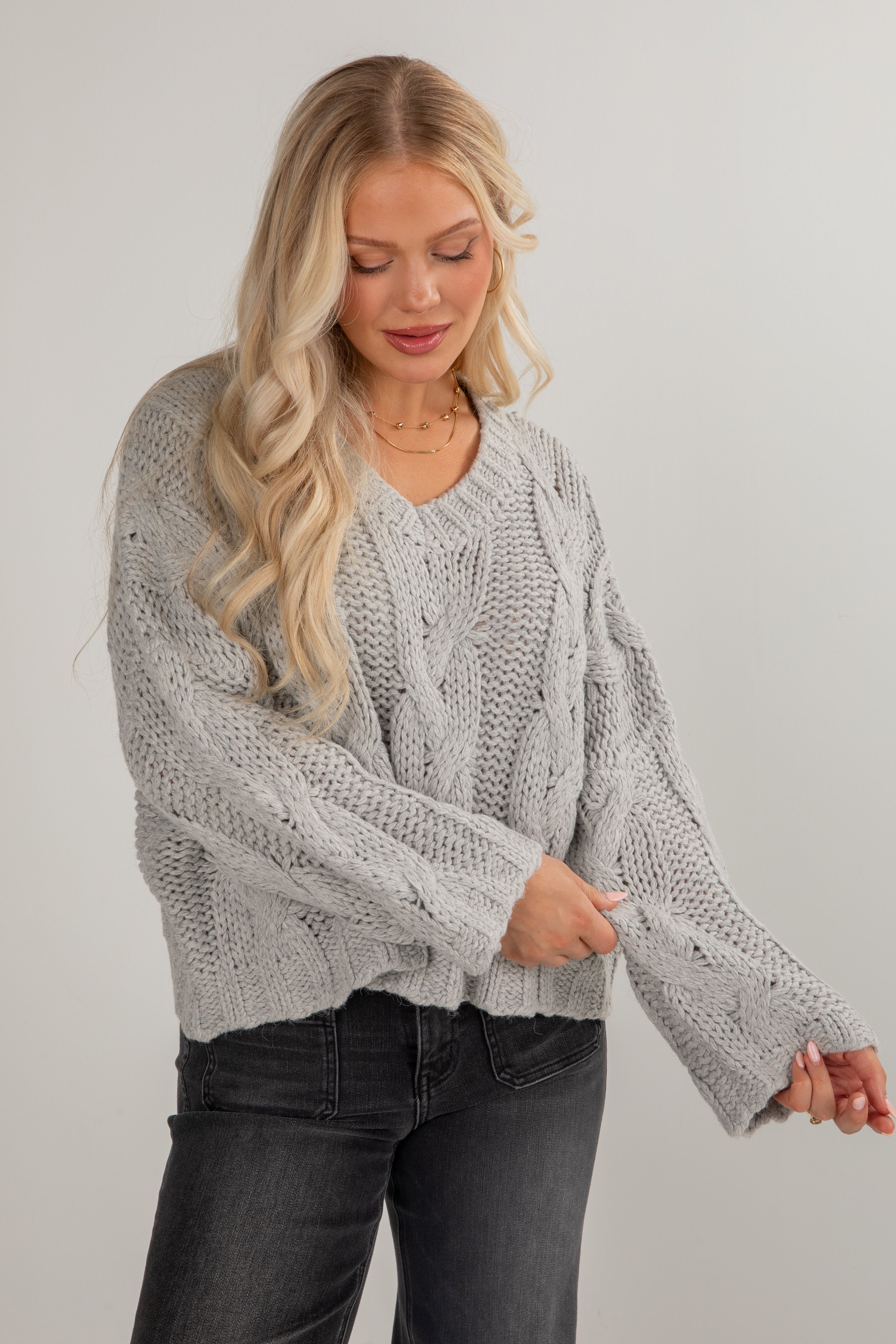 Woman wearing a gray cable knit sweater against a plain background