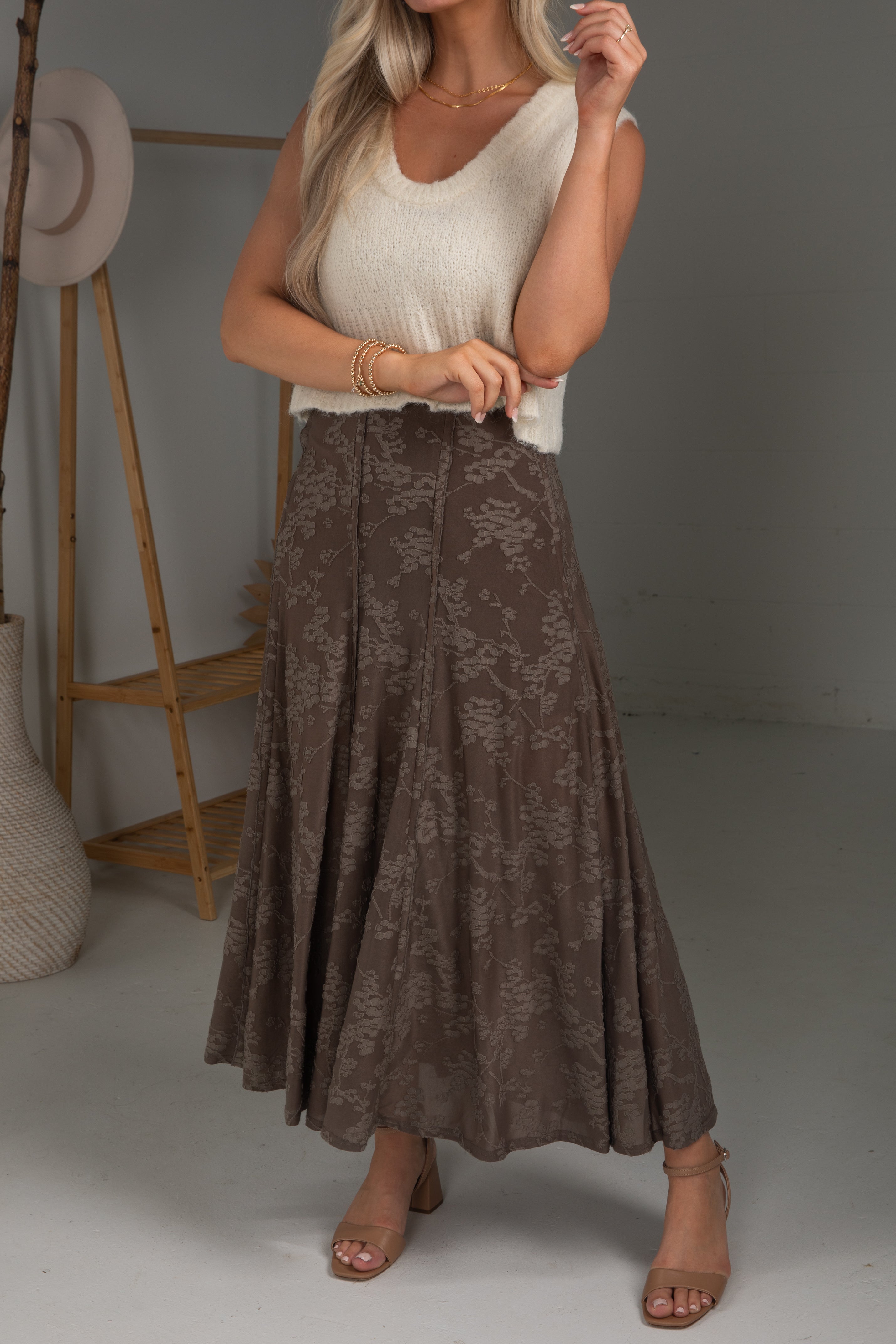 Woman wearing a white top and brown lace skirt in a neutral setting
