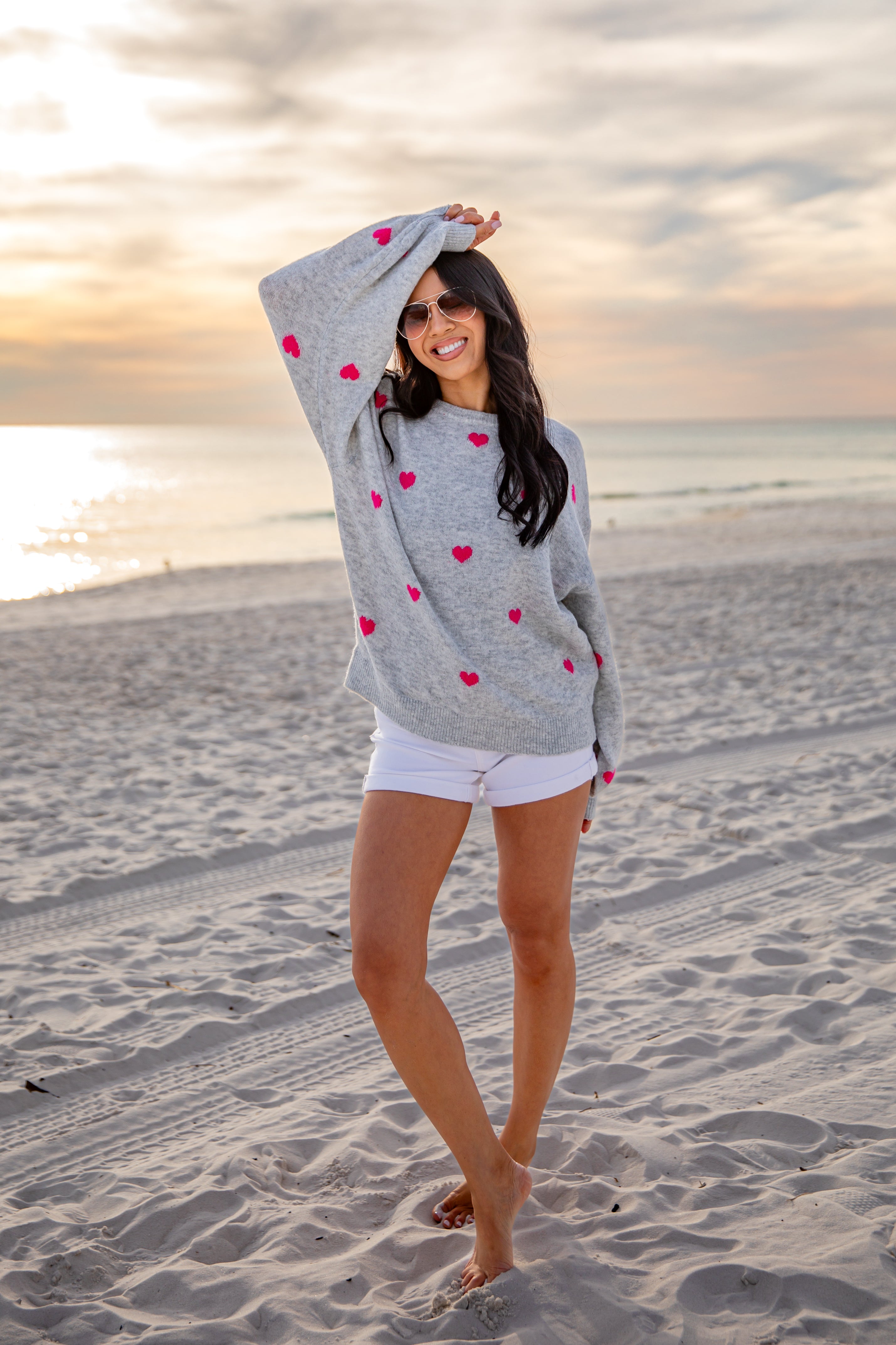 Woman in a gray sweater with red heart patterns on a beach at sunset