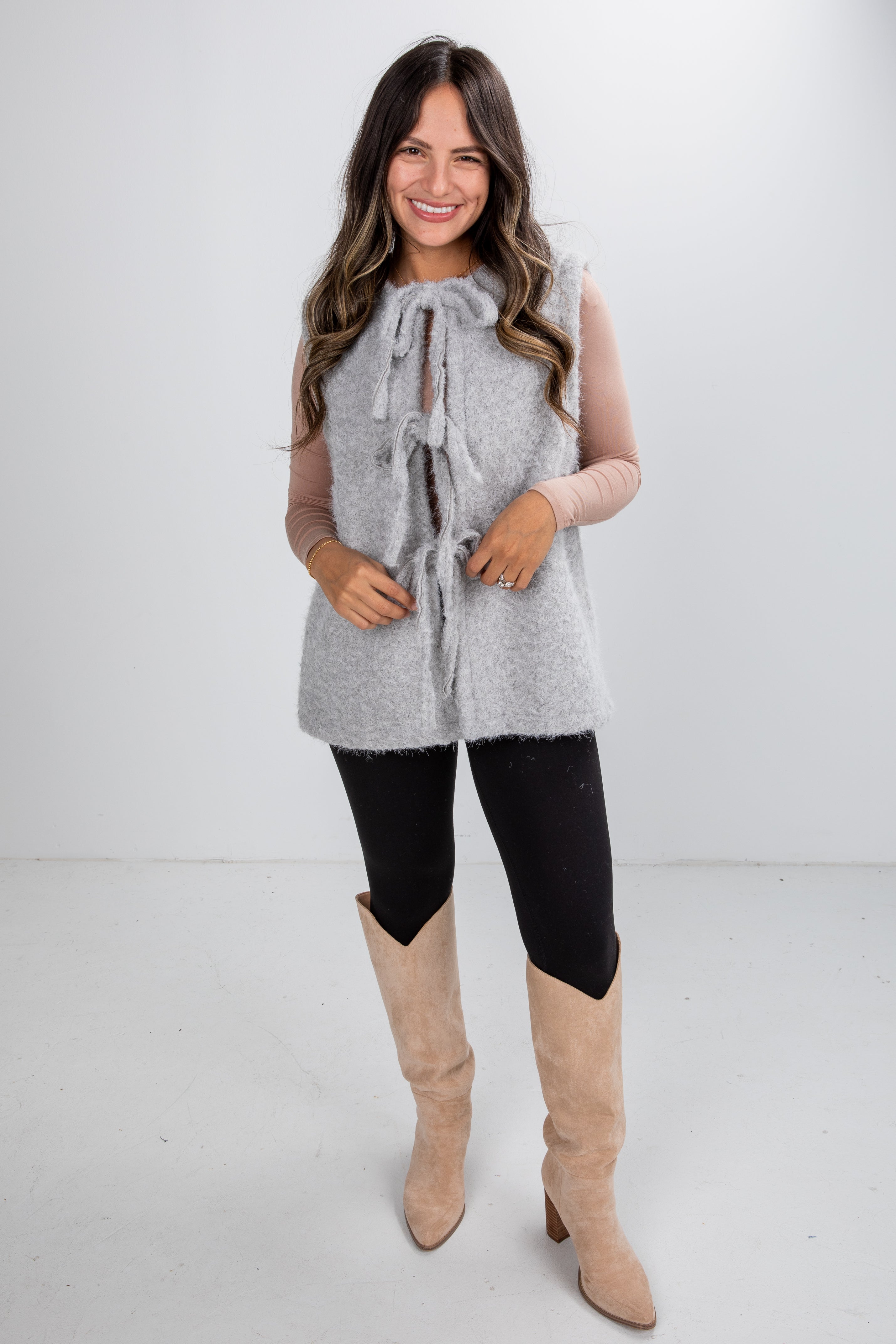 Woman wearing a gray sleeveless vest, black leggings, and beige knee-high boots on a white background