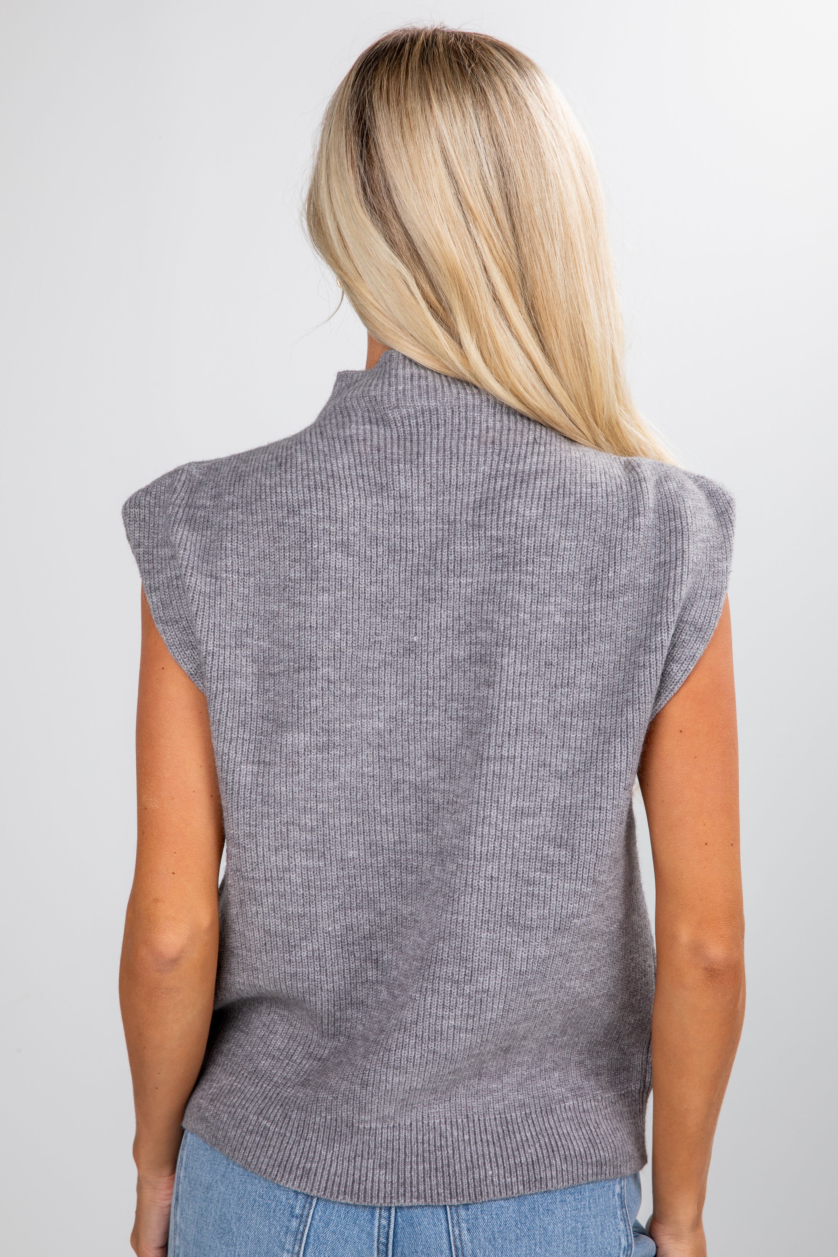 Person wearing a gray sleeveless sweater against a white background