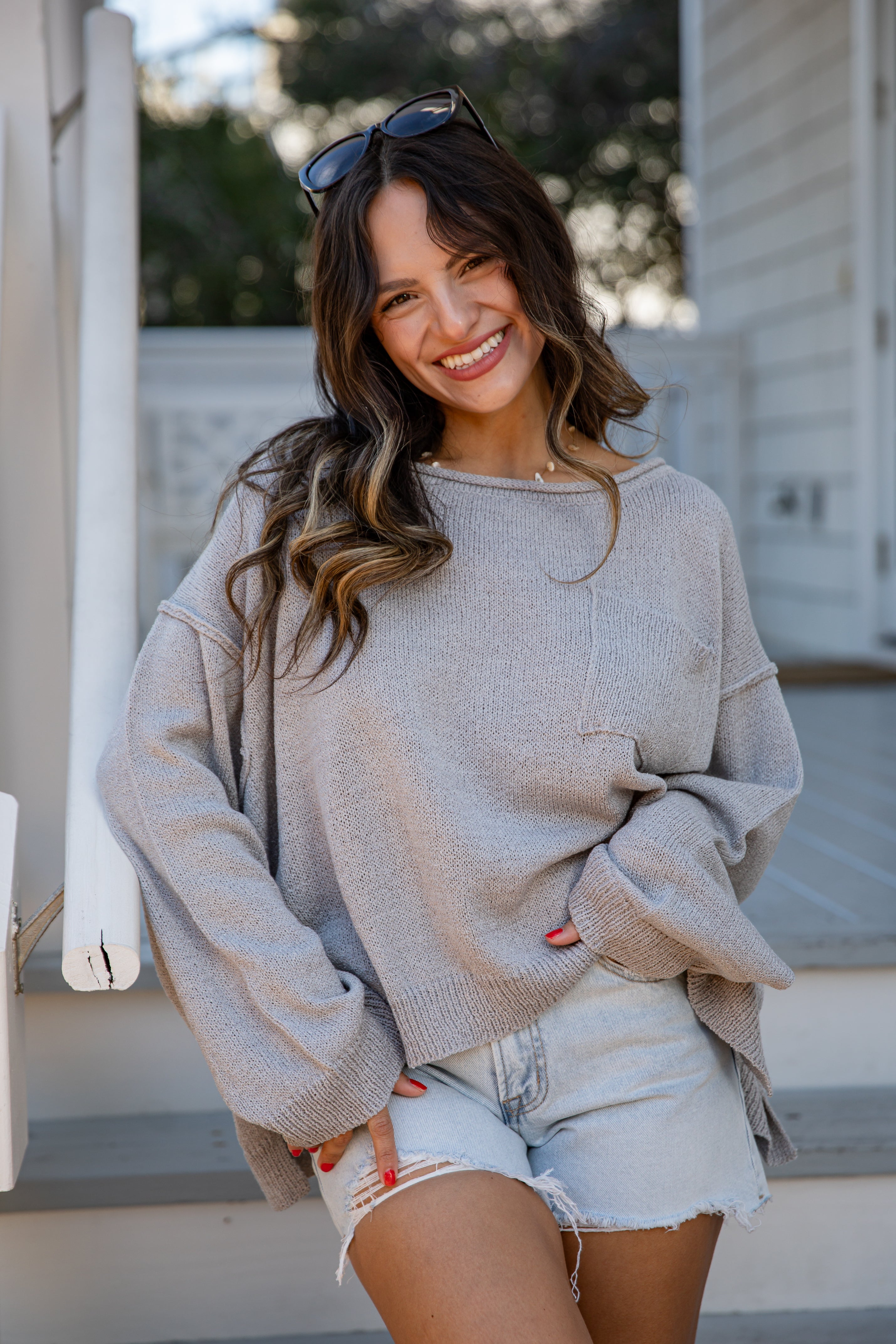 Woman wearing a beige sweater and denim shorts, standing outdoors.