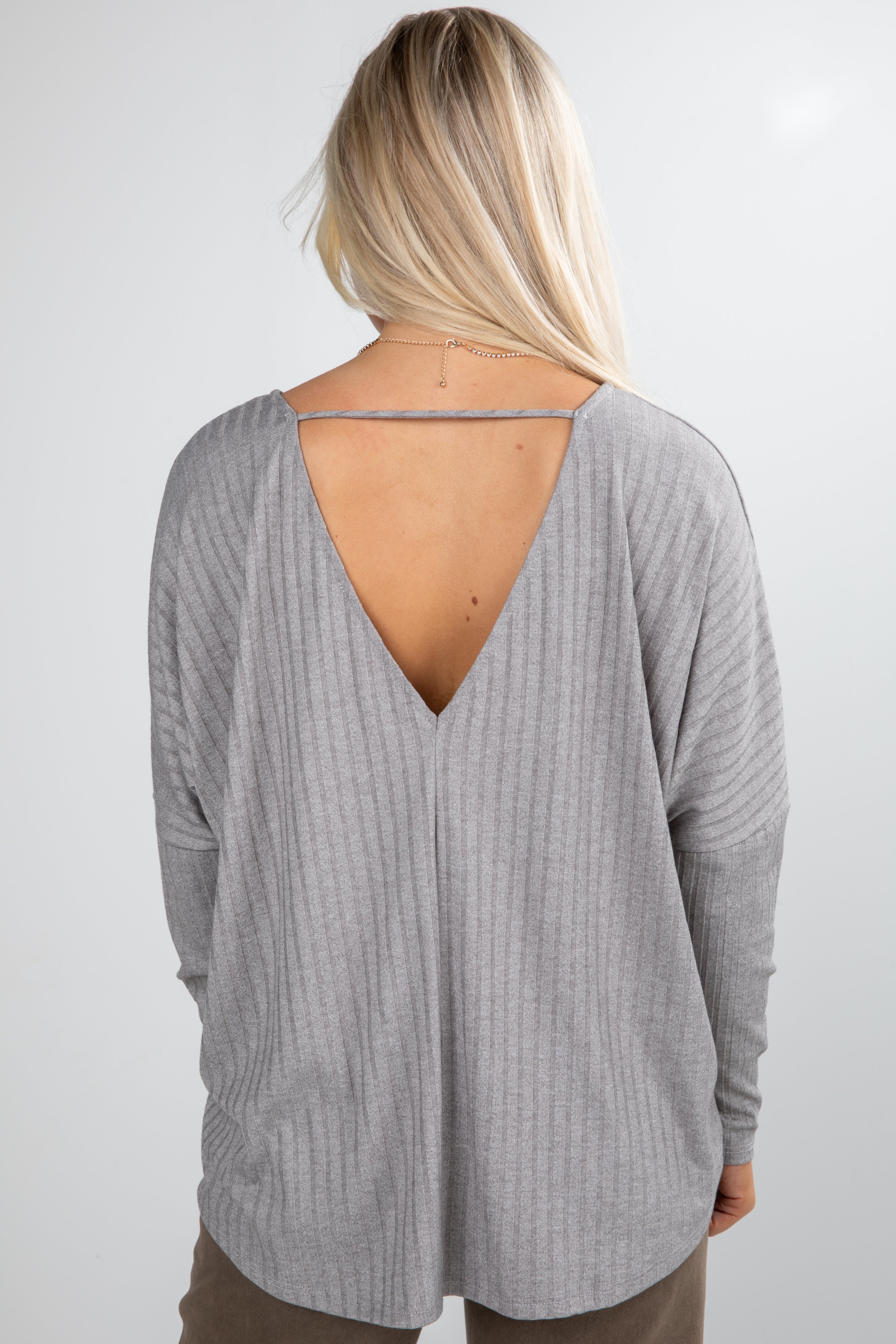 Person wearing a gray long-sleeve top with an open back on a white background