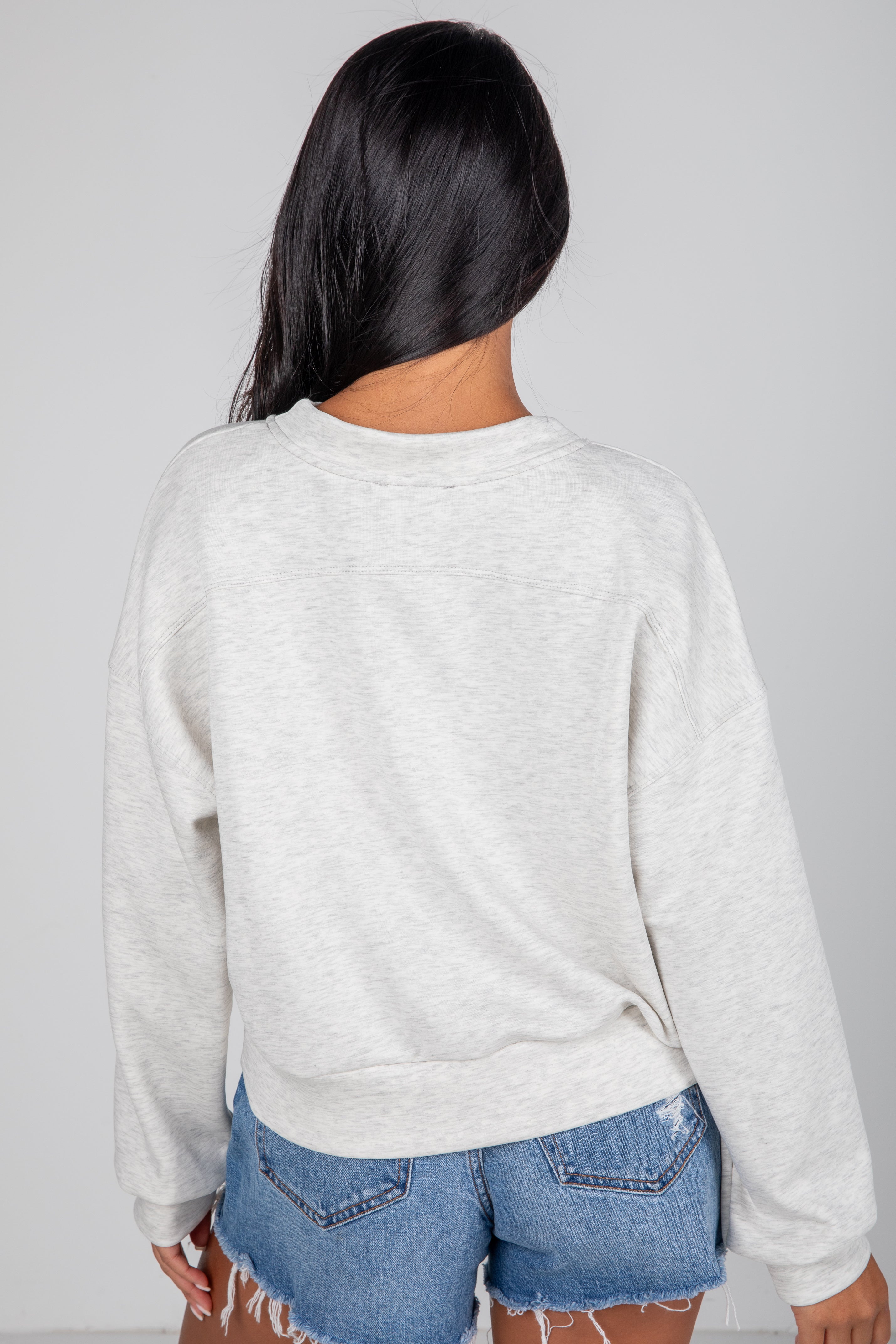 Person wearing a light gray sweatshirt and blue jeans on a plain background