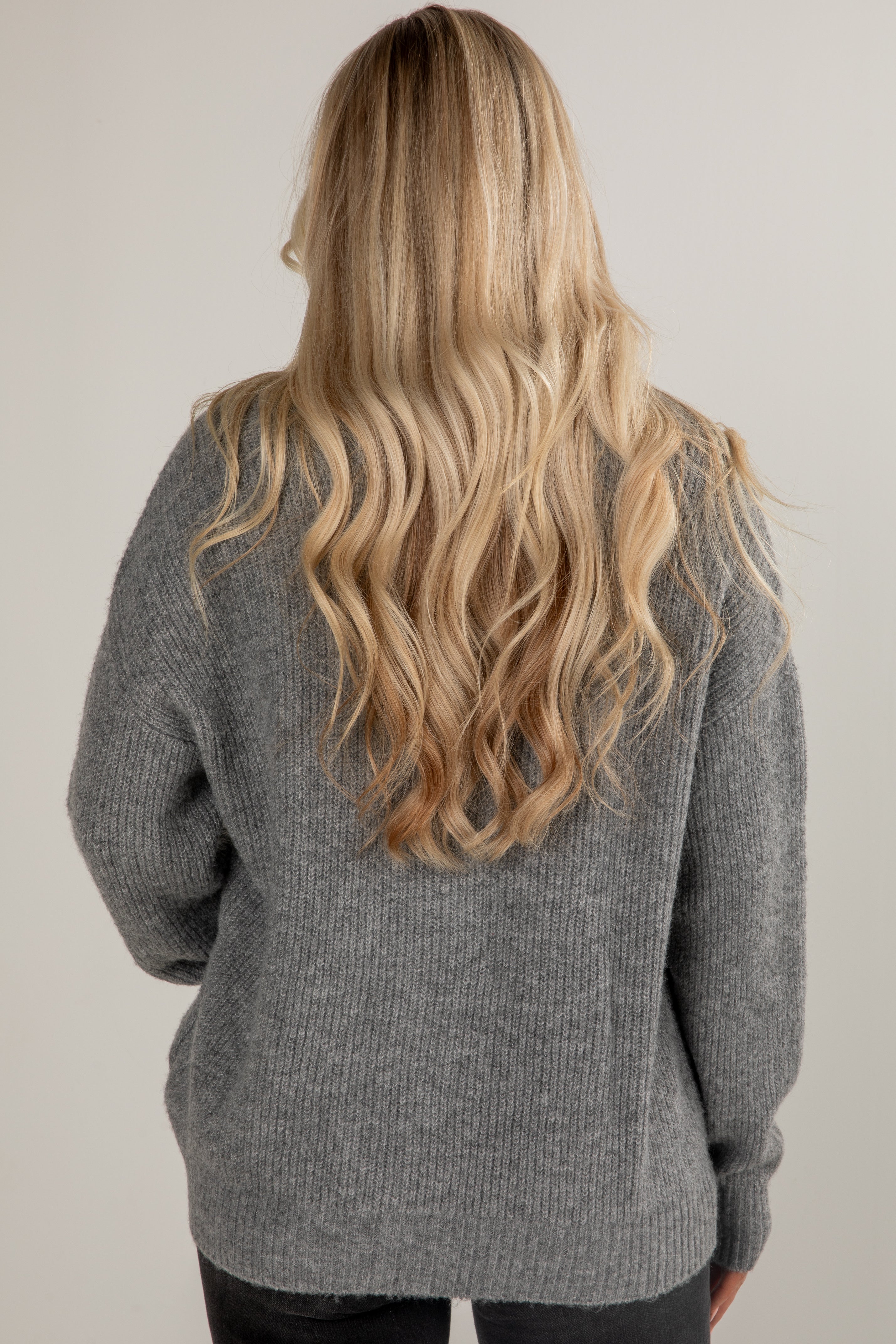 Person wearing a gray sweater with long blonde hair, standing against a plain background