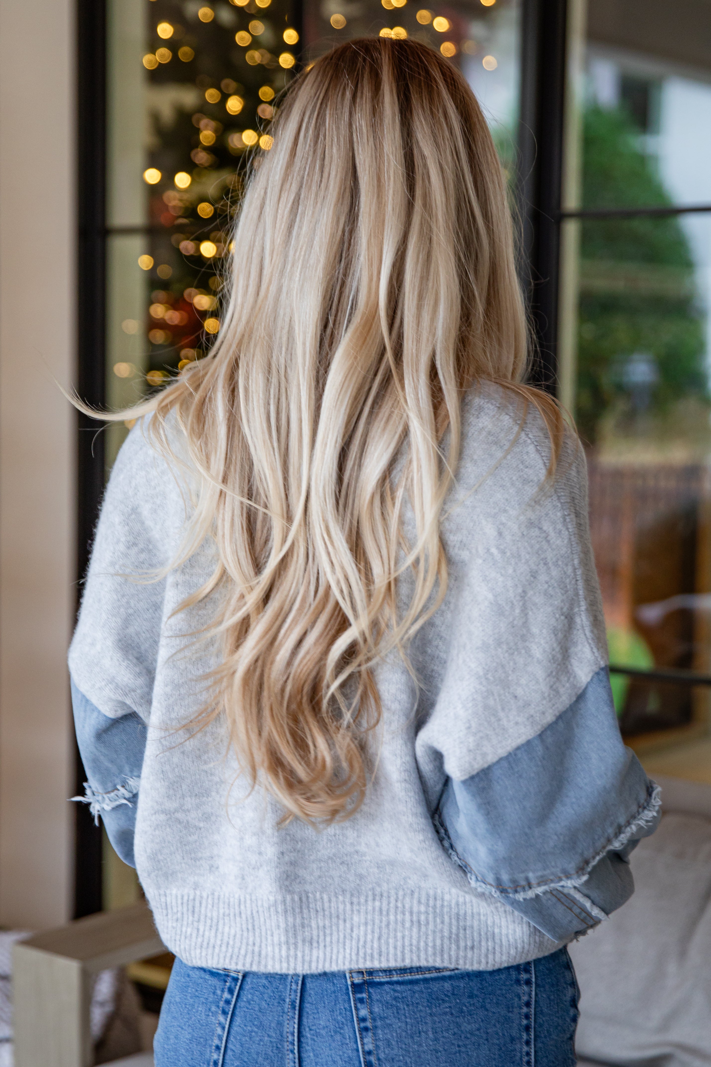 Person wearing a light gray sweater with denim sleeves in a cozy indoor setting.