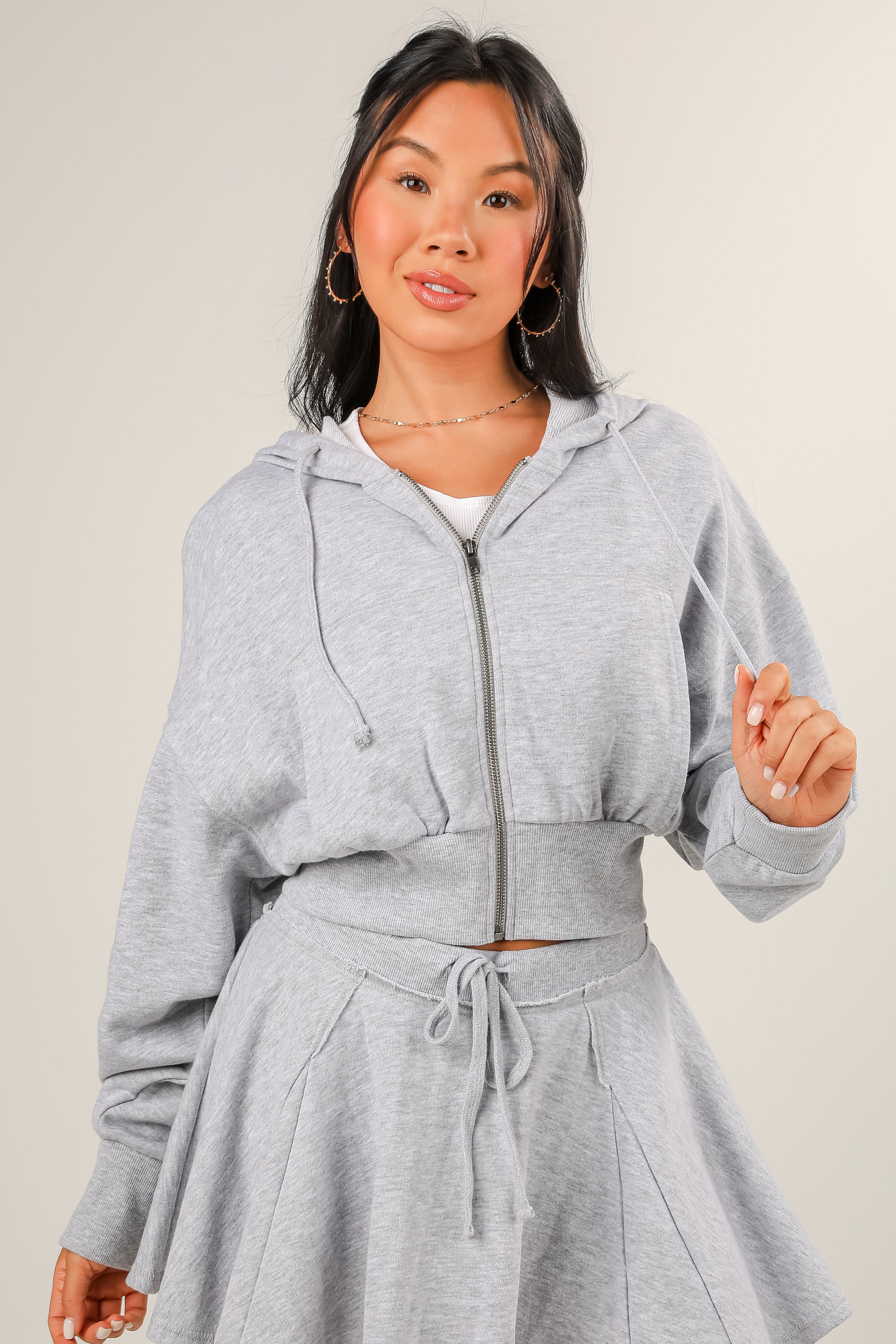 Woman wearing a gray hoodie and skirt set on a plain background