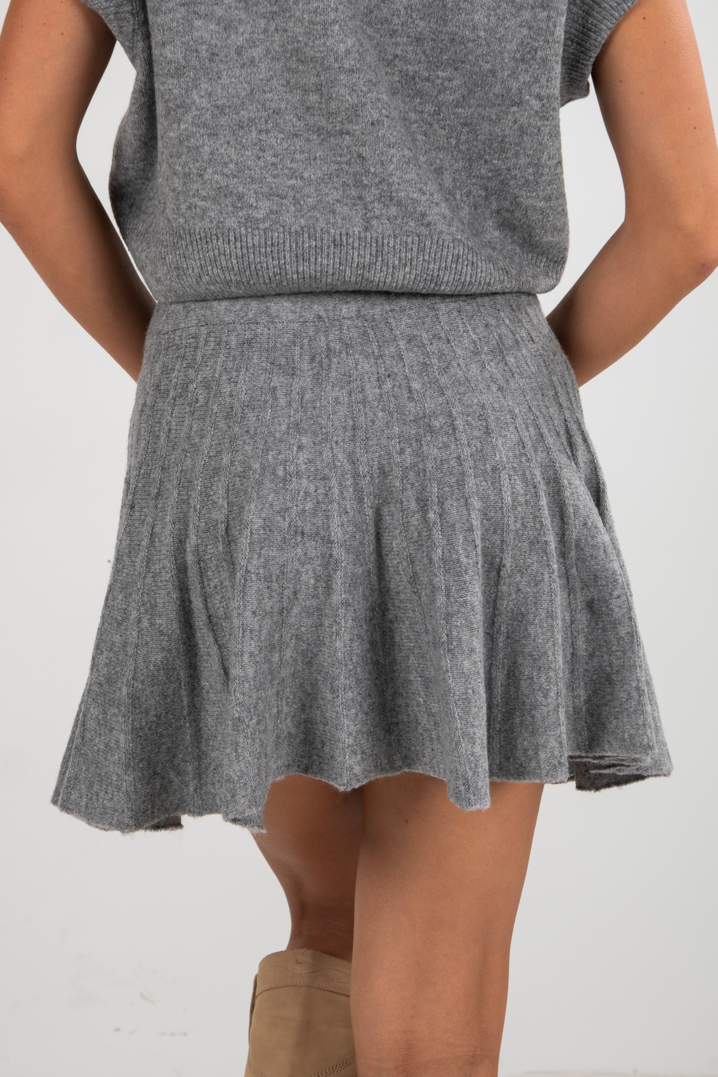 Person wearing a gray knit skirt and sleeveless top on a white background