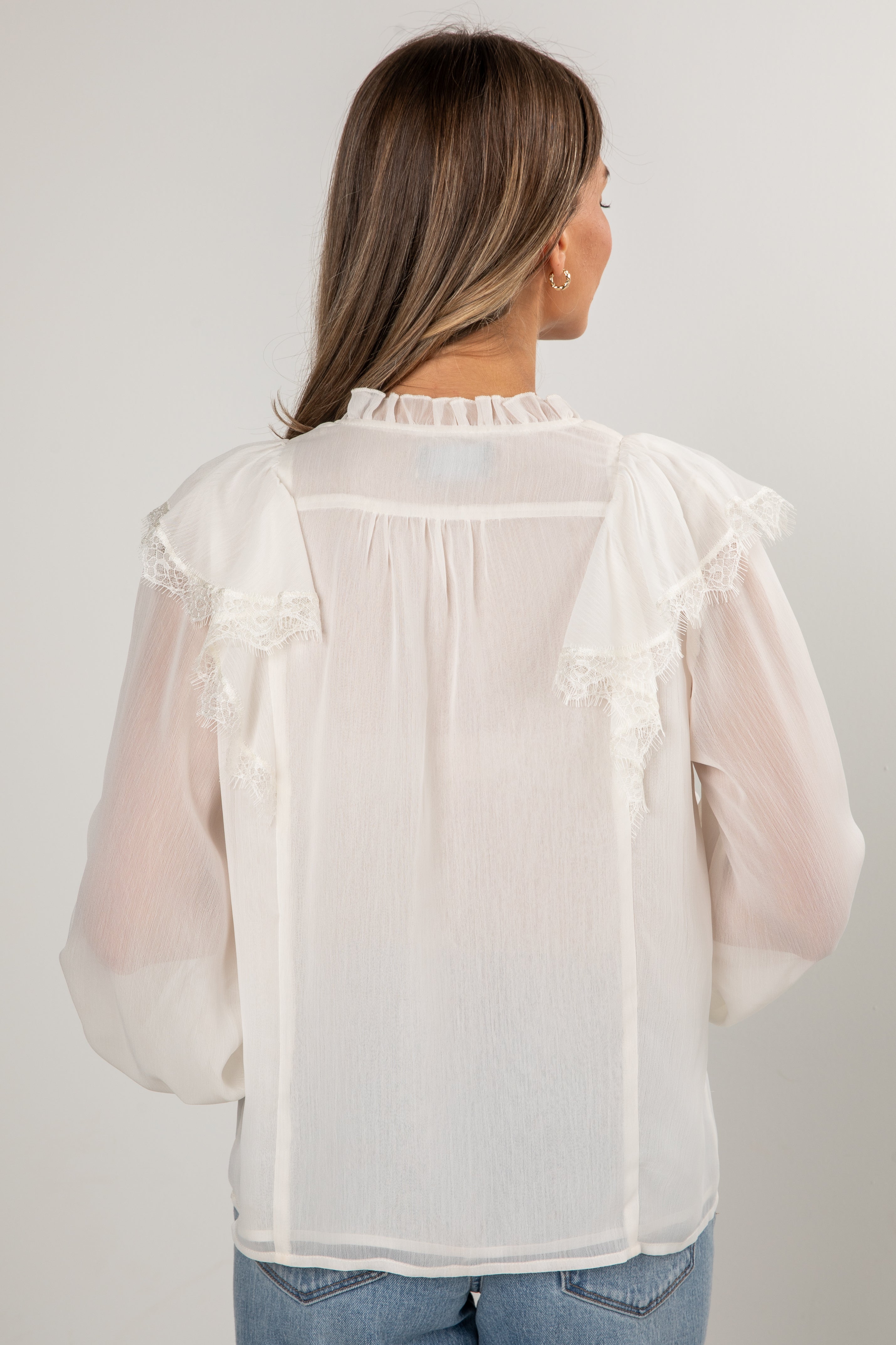 Woman wearing a sheer white blouse with long sleeves against a plain background
