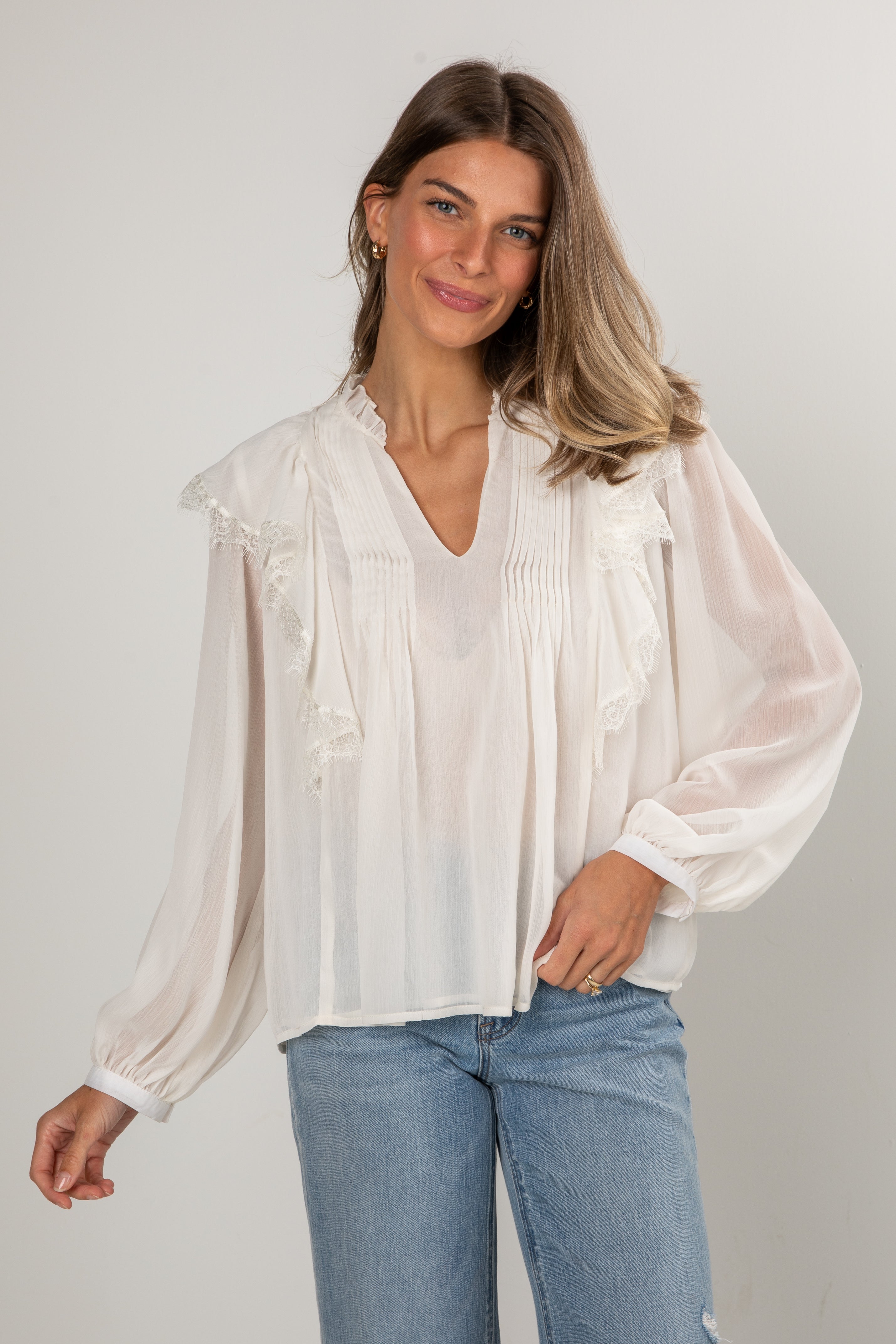 Woman wearing a white blouse with sheer sleeves against a plain background