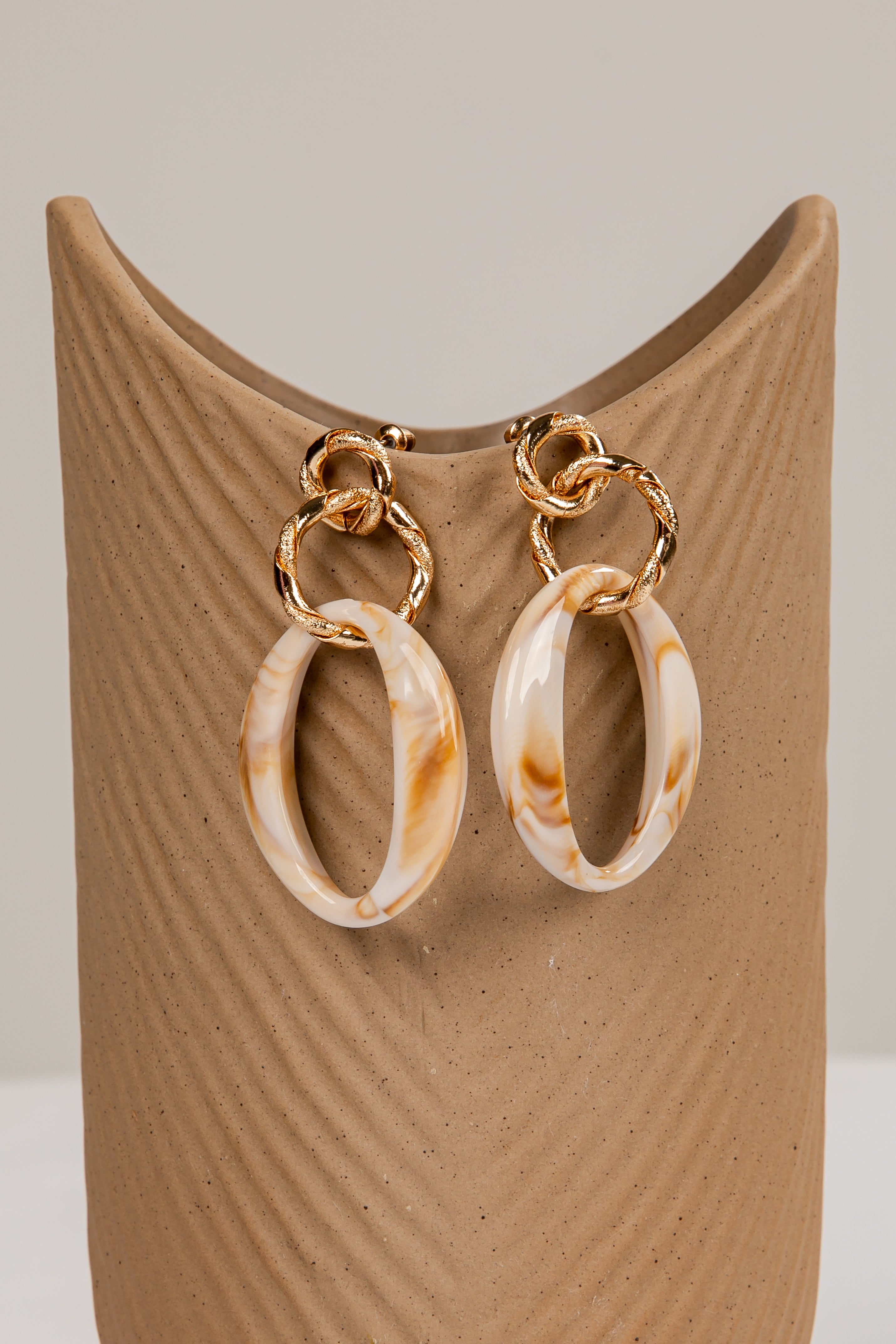 Pair of gold and marbled beige hoop earrings on a brown stand.
