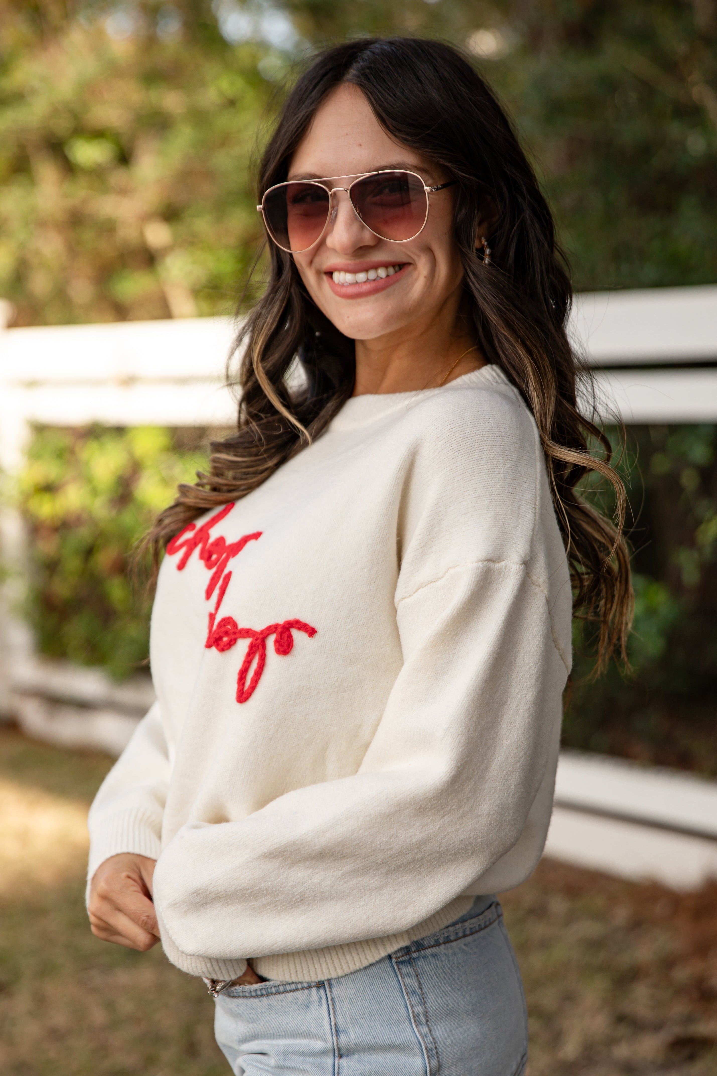 Woman wearing a white sweater with red text outdoors