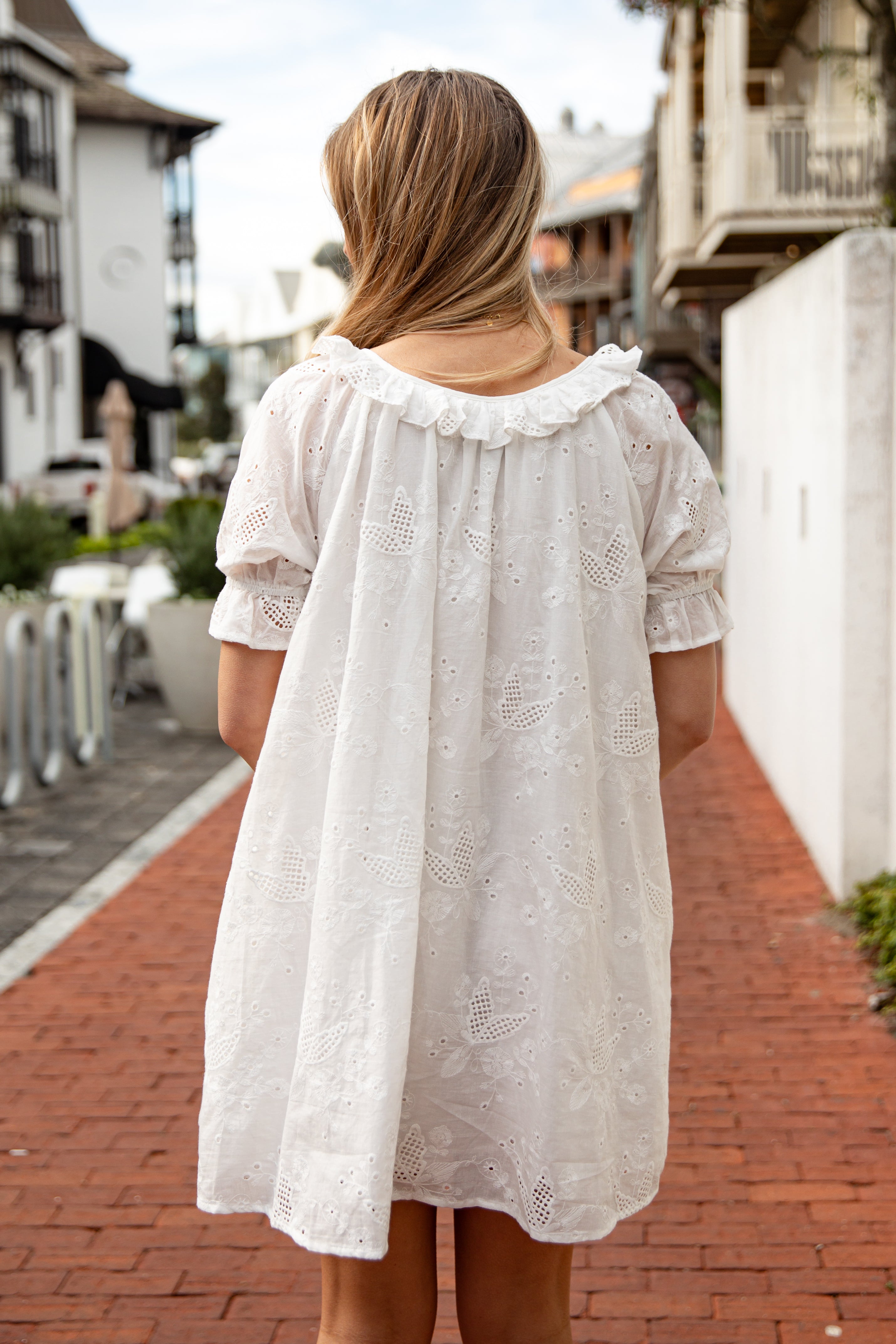 Woman wearing a white lace dress walking on a brick path with buildings in the background