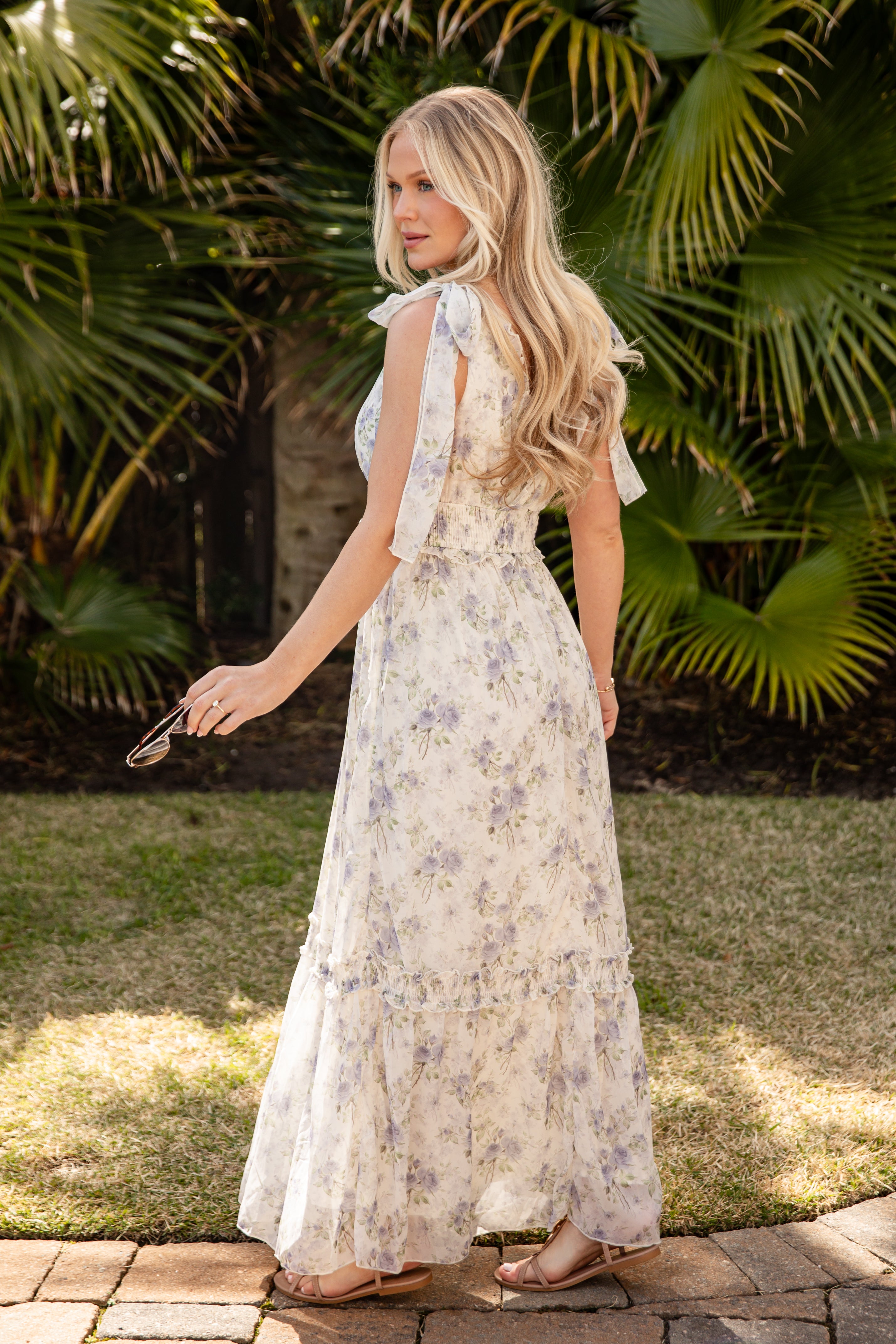 Woman in a floral dress standing outdoors with greenery in the background
