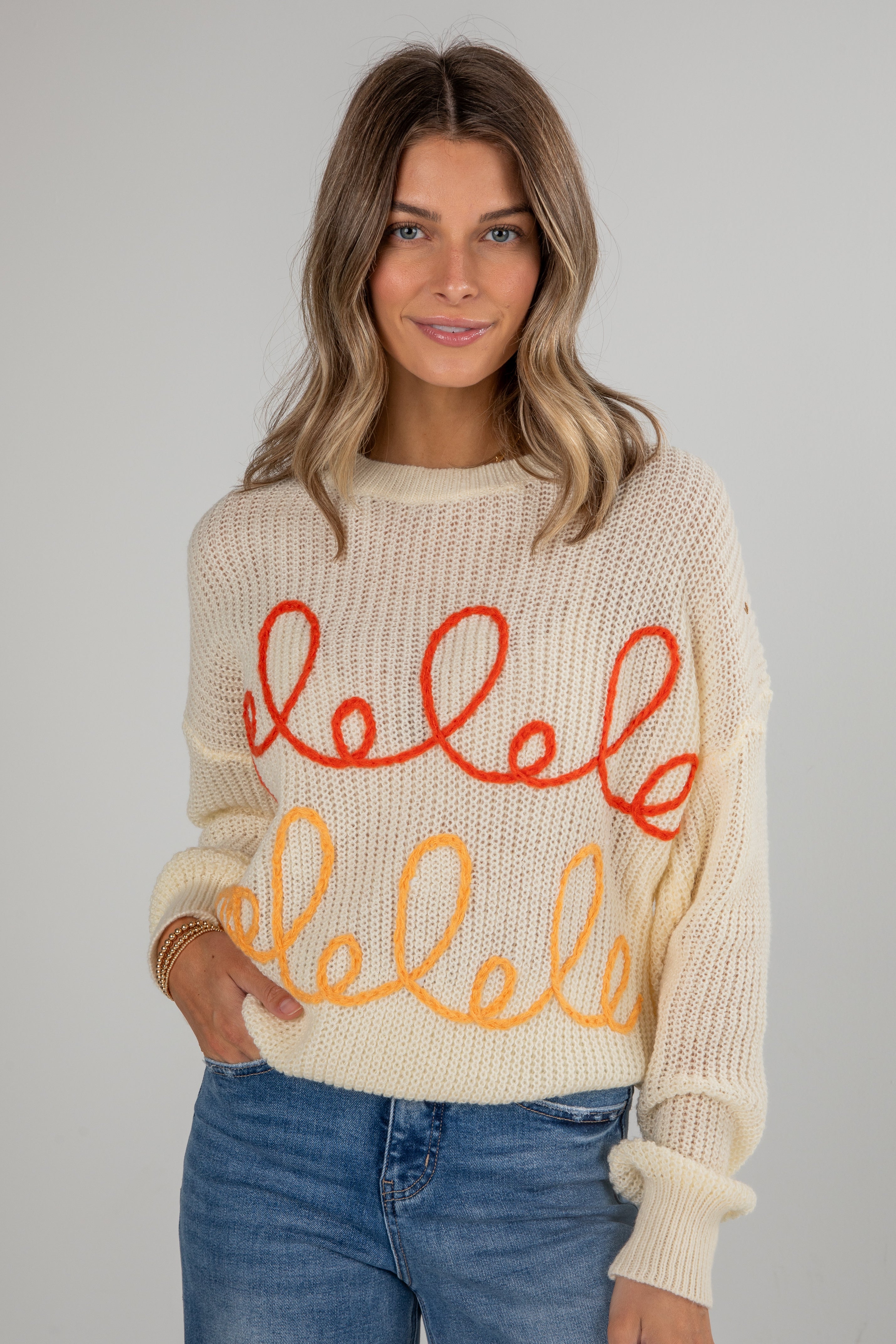 Woman wearing a cream sweater with red and orange text on a plain background