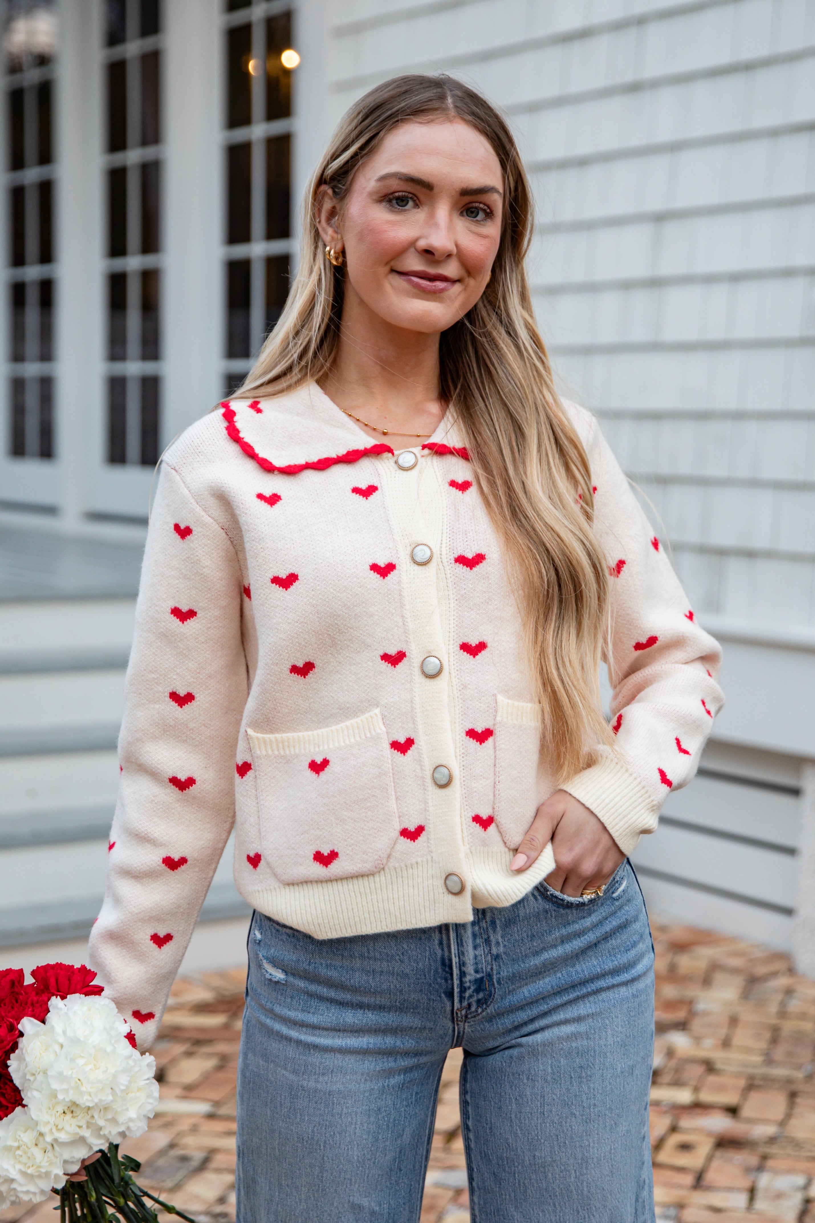 Woman wearing a cream cardigan with red heart patterns, standing outdoors.