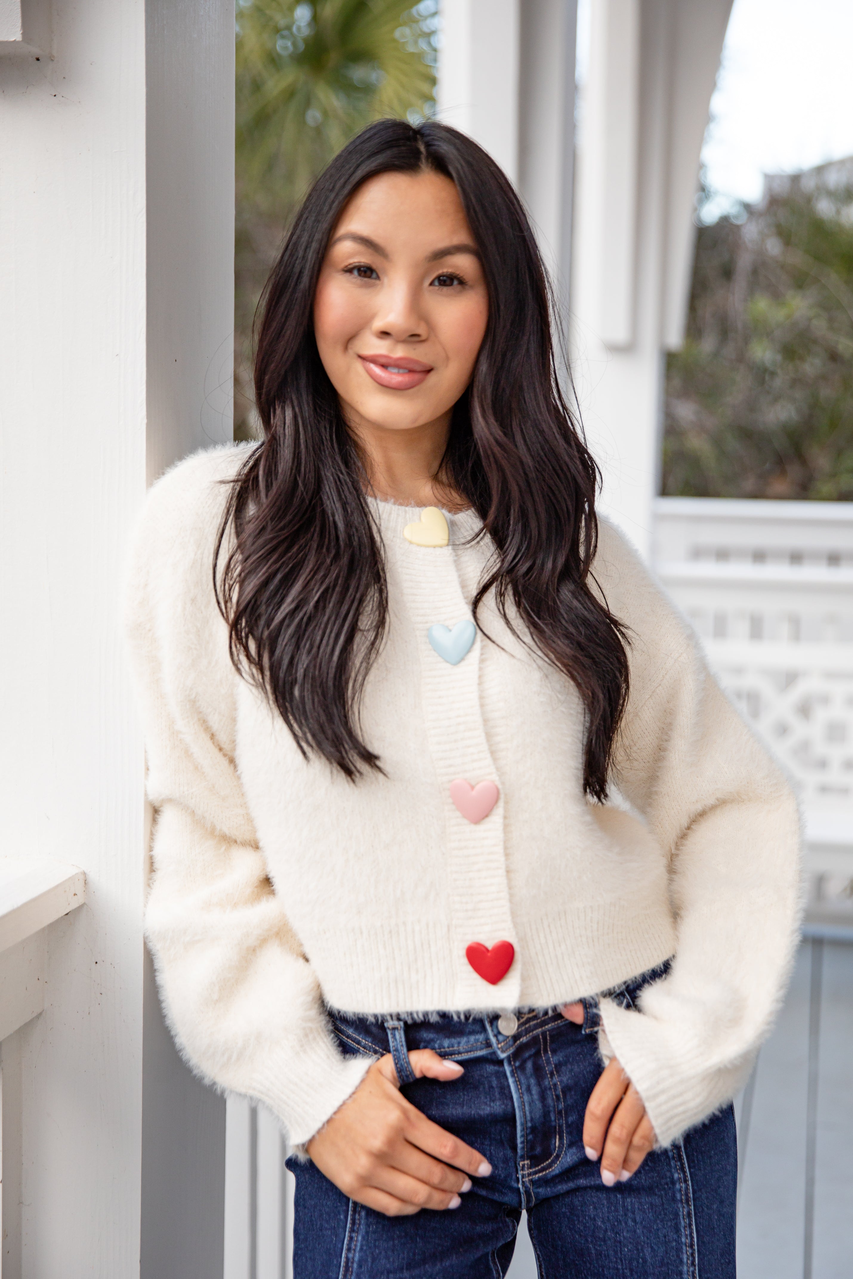 Woman wearing a cream-colored sweater with heart patterns, standing outdoors.