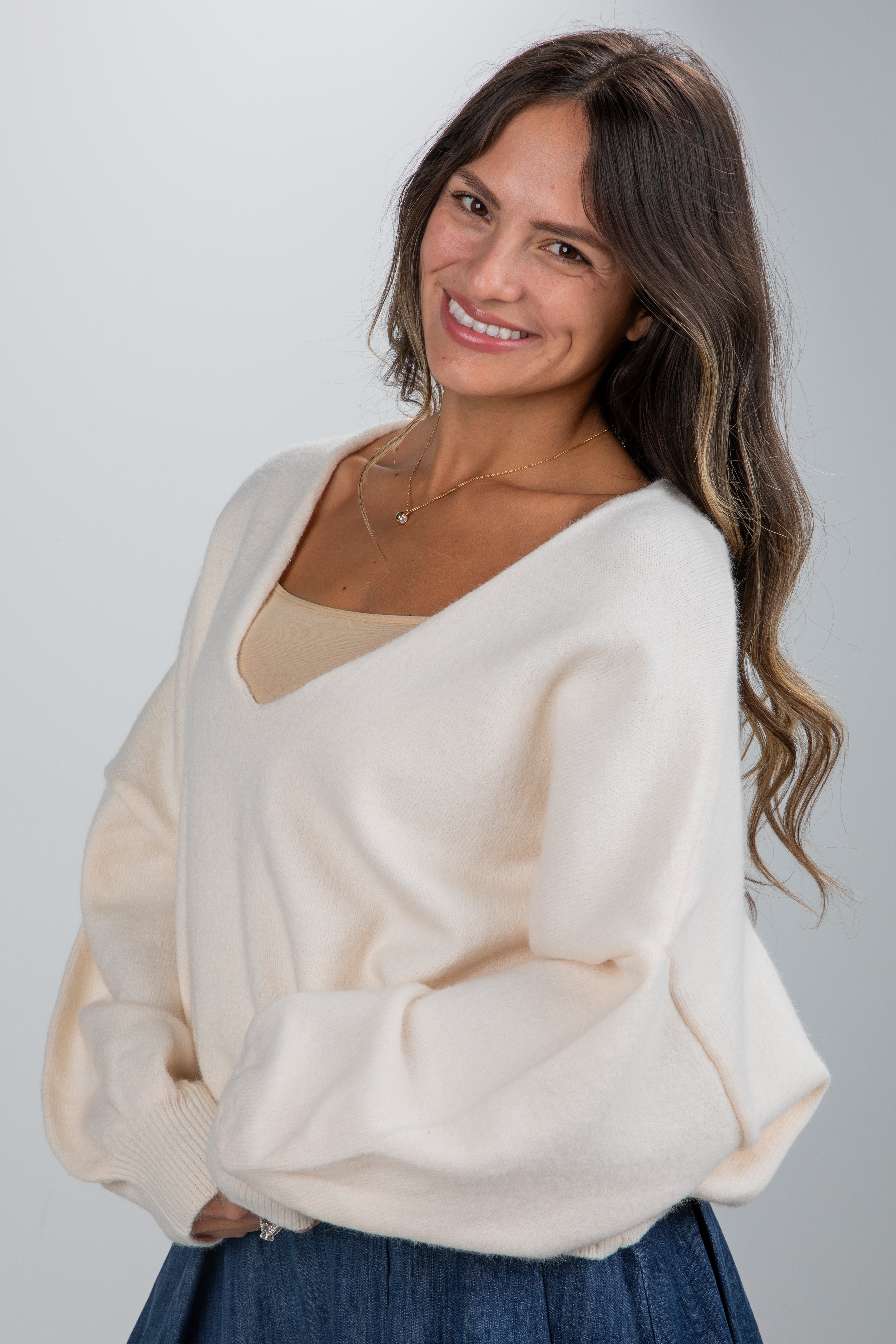 Woman wearing a beige sweater and blue skirt against a plain background
