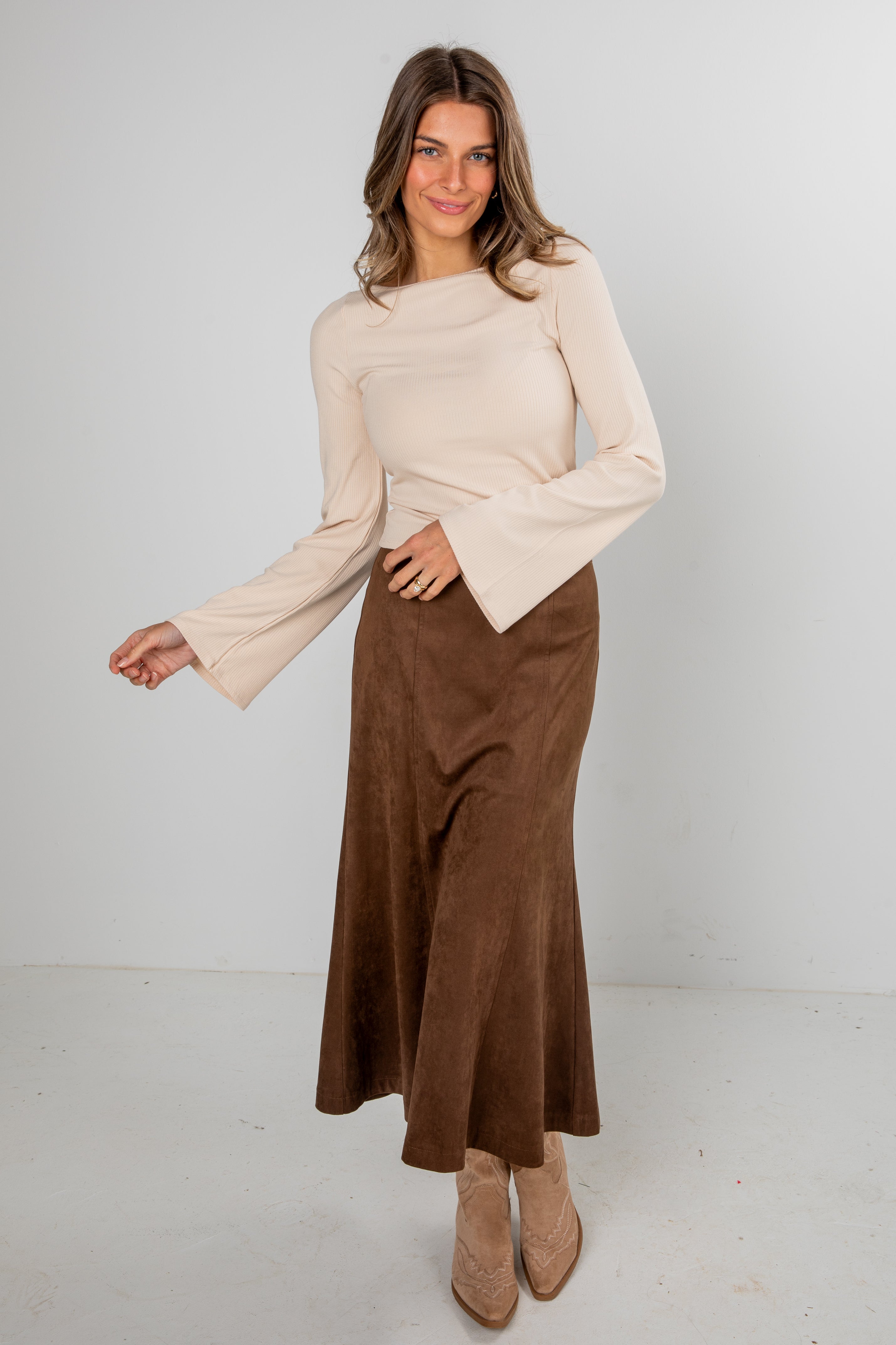 Woman wearing a beige top and brown skirt against a white background